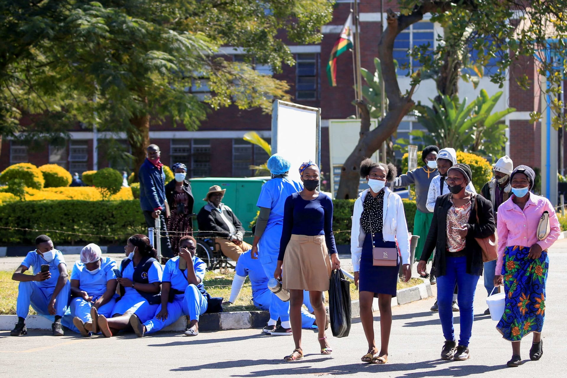 <p>People walk past Zimbabwean medical workers as they sit outside Sally Mugabe Hospital during a strike by state doctors and nurses for higher pay, in Harare, Zimbabwe, June 20, 2022.</p>
