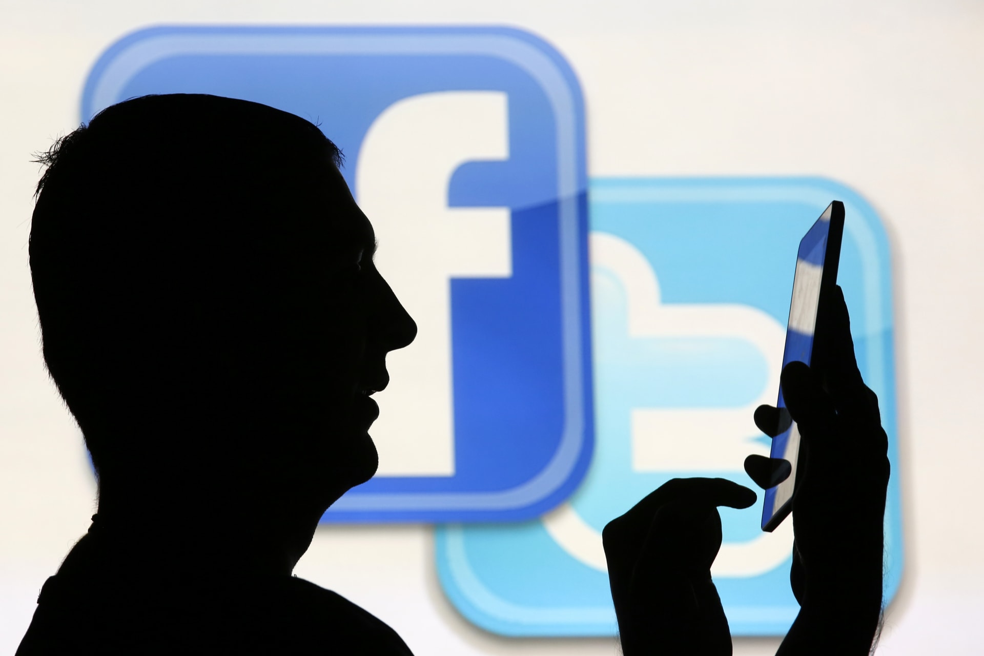 <p>Man uses tablet computer while standing in front of video screen with Facebook and Twitter logos in this picture illustration taken in Sarajevo</p>
