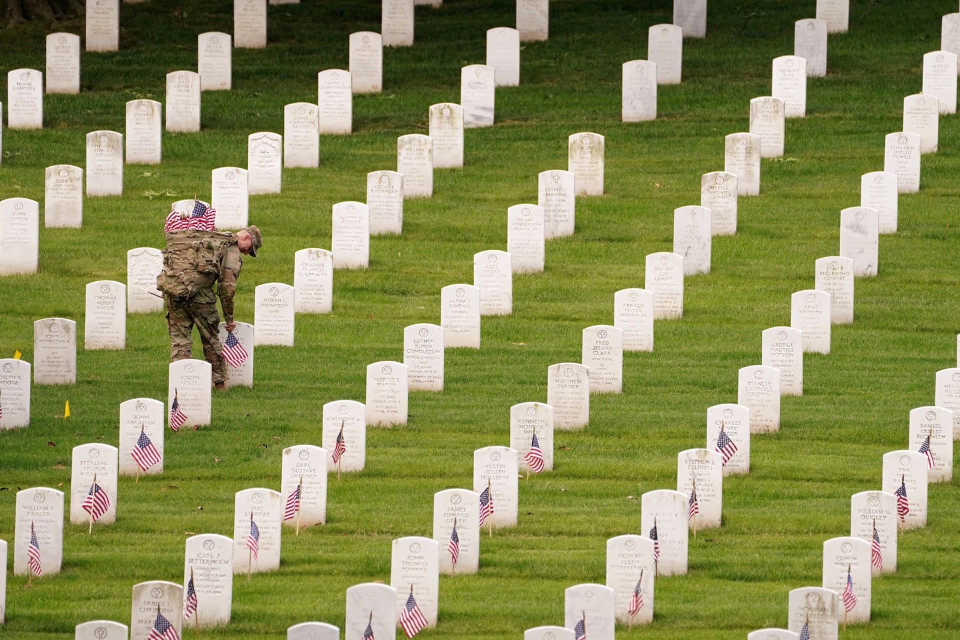 <p>A soldier of the 3rd U.S. Infantry Regiment places flags on headstones in Arlington National Cemetery ahead of Memorial Day on May 26, 2022. </p>
