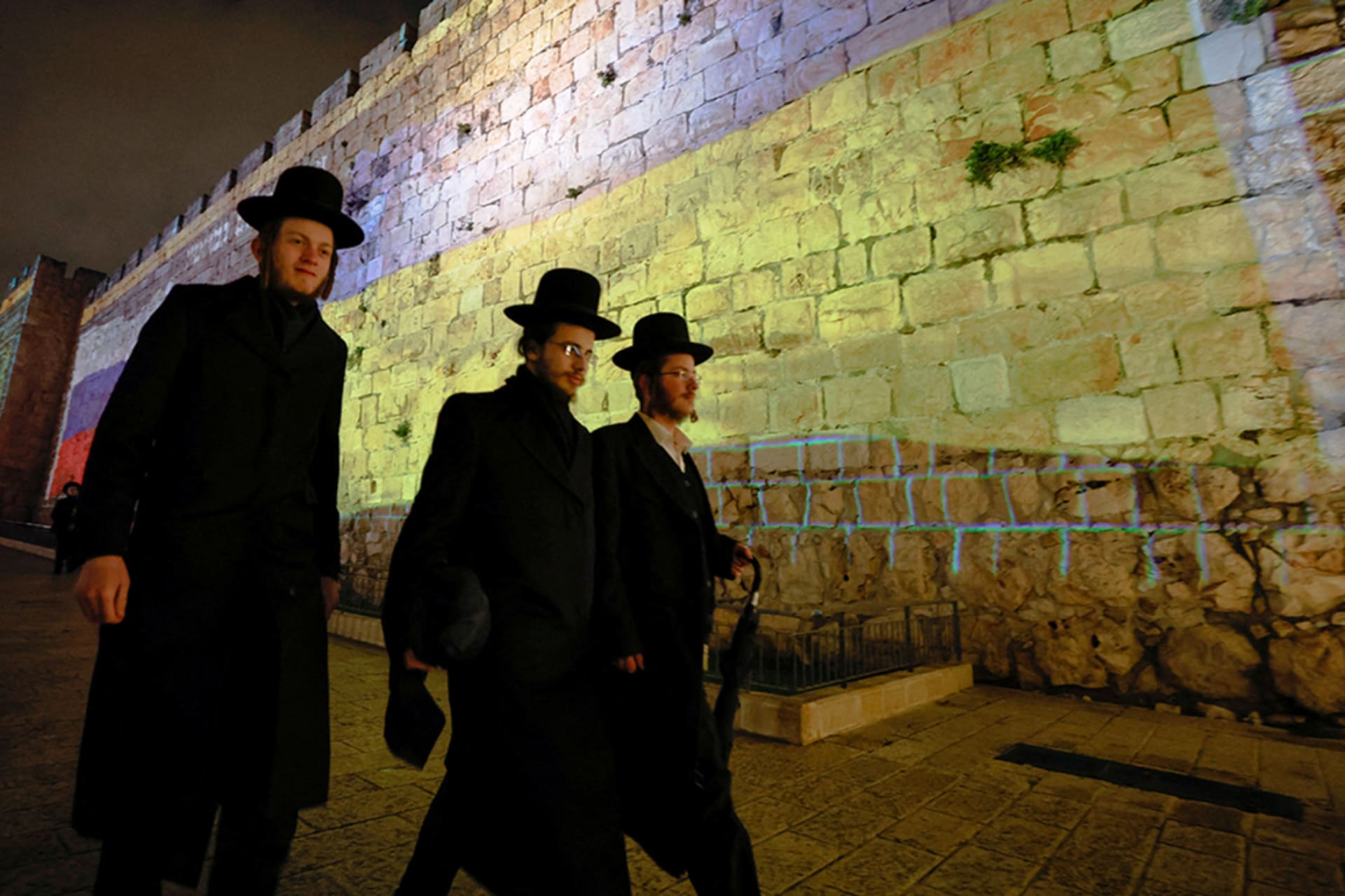 <p>People walk past projections of the national flags of Russia and Ukraine on the walls of Jerusalem’s Old City.</p>
