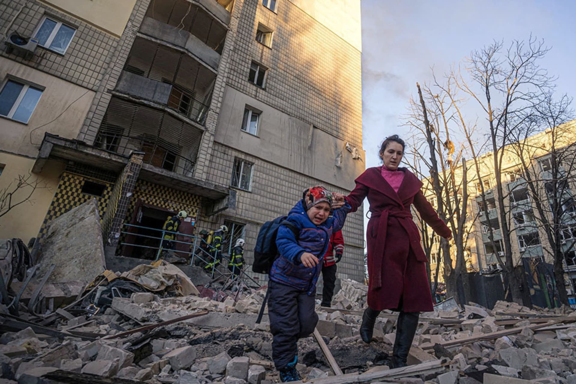 <p>A woman with a child evacuates from a residential building damaged by shelling by Russian forces in Kyiv, Ukraine, in March 2022.</p>