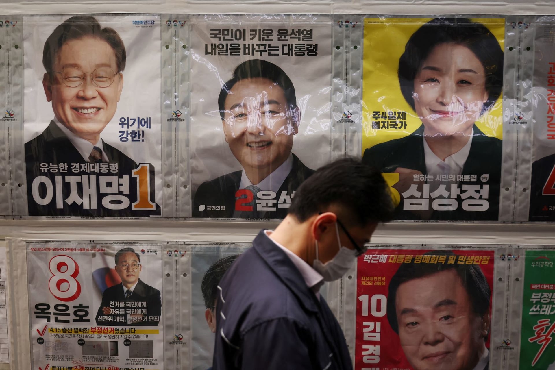 <p>A man stands in front of posters of candidates for the upcoming March 9 presidential election as he queues to cast his early vote at a polling station in Seoul, South Korea on March 4, 2022.</p>