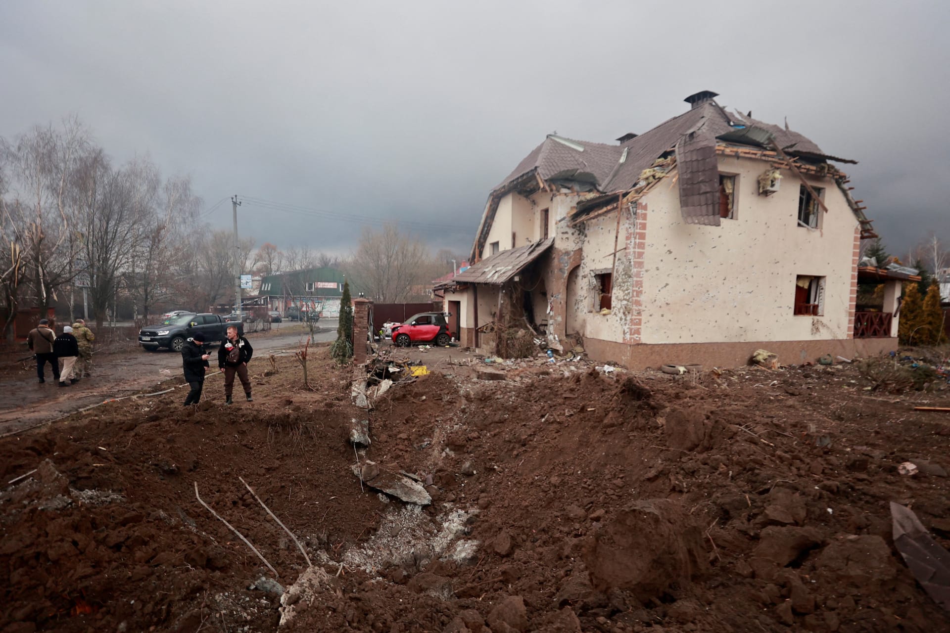 <p>People stand next to a shell crater in front of a house damaged by recent shelling in the village of Hatne, in the Kyiv region, on March 3, 2022. </p>
