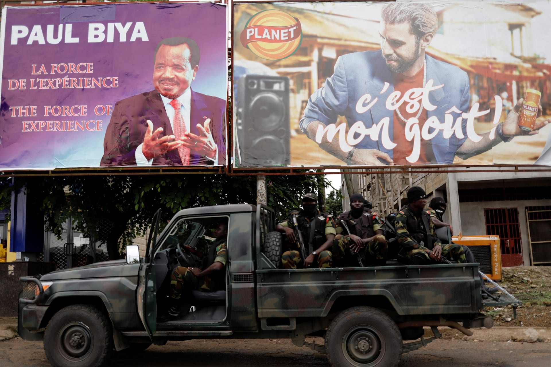 <p>Cameroonian elite Rapid Intervention Battalion members sit on their military vehicle under an electoral billboard of Cameroon President Paul Biya during a patrol in the south west city of Buea, Cameroon on October 4, 2018.</p>

