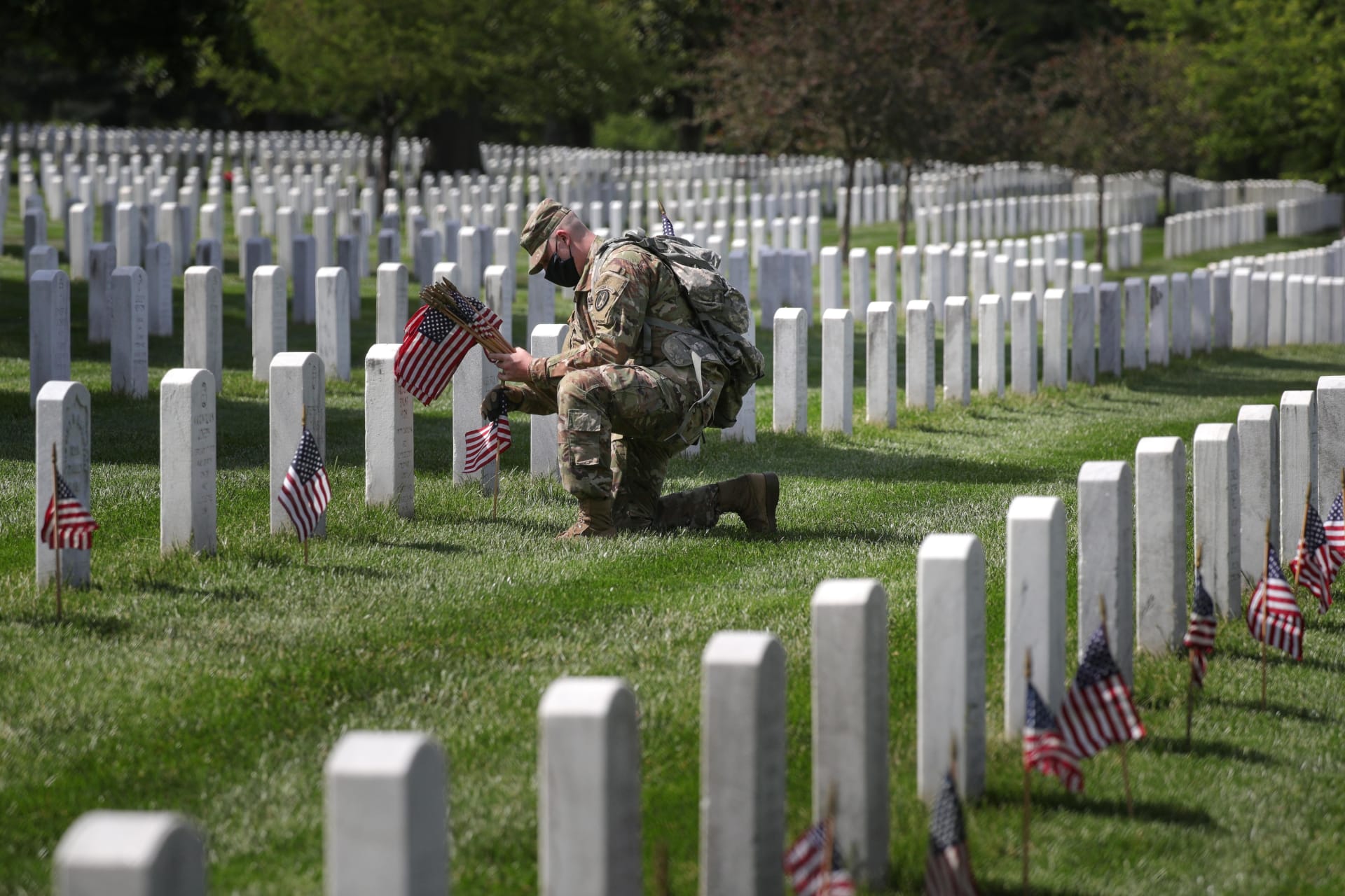 <p>A member of the U.S. Army Old Guard places American flags near headstones at Arlington National Cemetery on May 21, 2020.</p>
