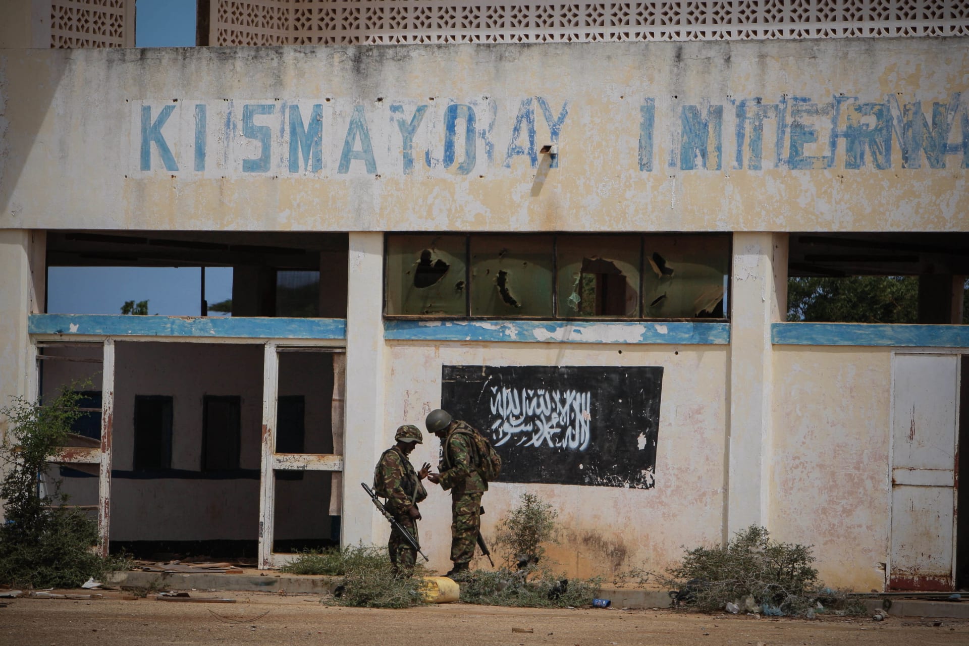 <p>Soldiers of the Kenyan Contingent serving with the African Union Mission in Somalia (AMISOM) stand in front of the black flag of the al Qaeda-affiliated extremist group Al Shabab painted on the wall of Kismayo Airport on October 2, 2012.</p>
