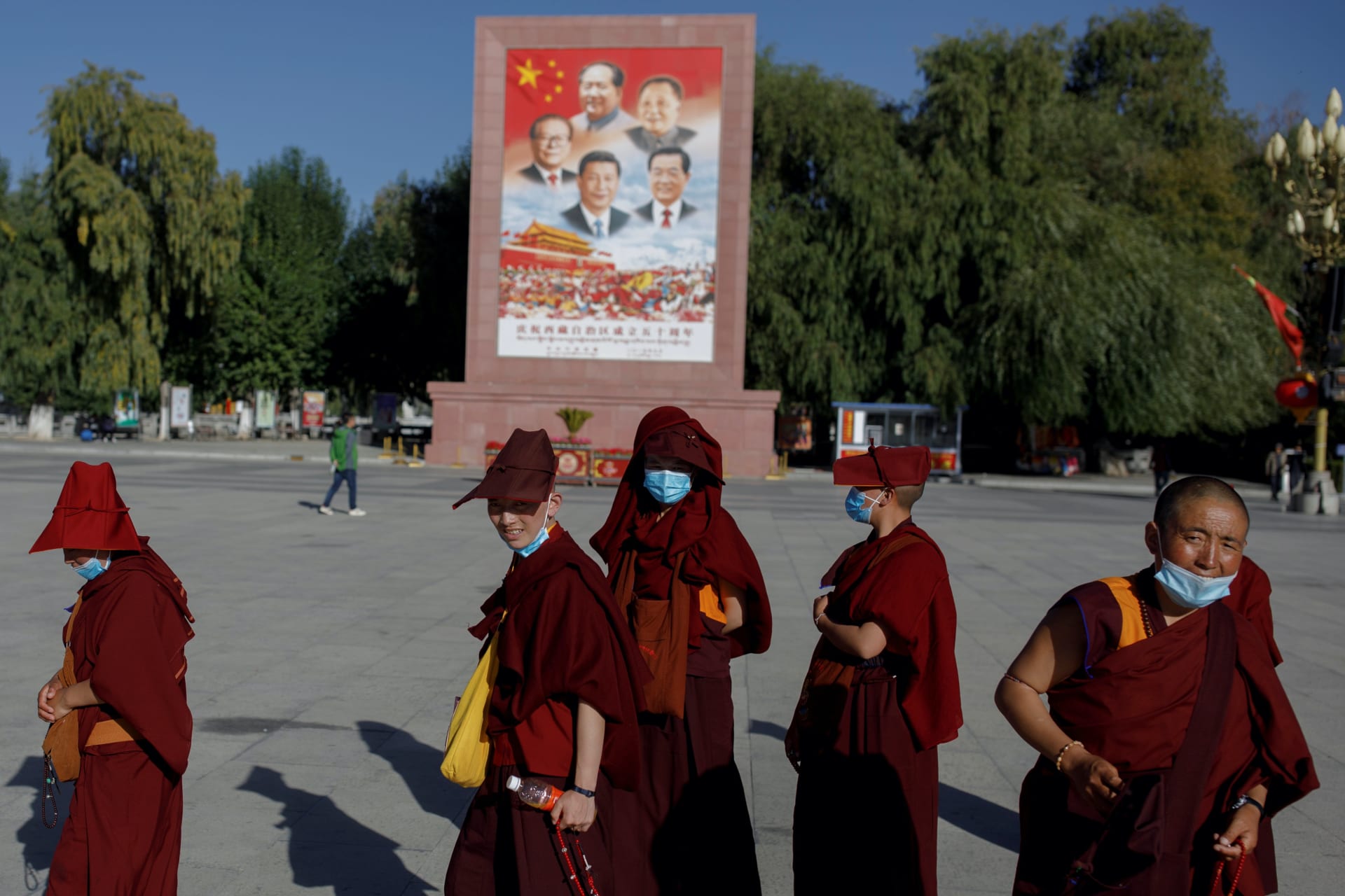 <p>Tibetan Buddhists walk past a poster showing Chinese President Xi Jinping and former Chinese leaders Jiang Zemin, Mao Zedong, Deng Xiaoping, and Hu Jintao during a government-organized tour of Tibet on October 15, 2020.</p>
