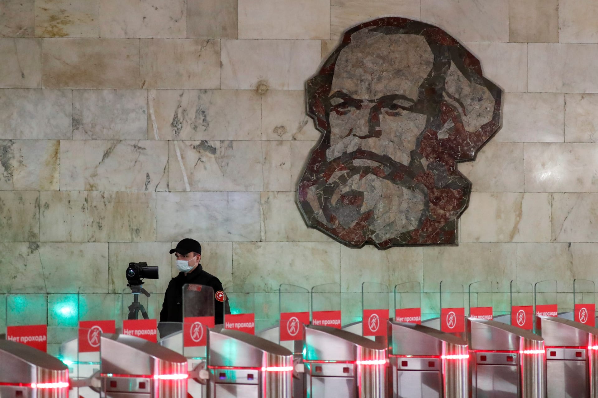 <p>An employee wearing a protective mask uses a device to take passengers’ body temperature near a mosaic artwork, which depicts German philosopher Karl Marx, at an entrance to a metro station in central Moscow.</p>
