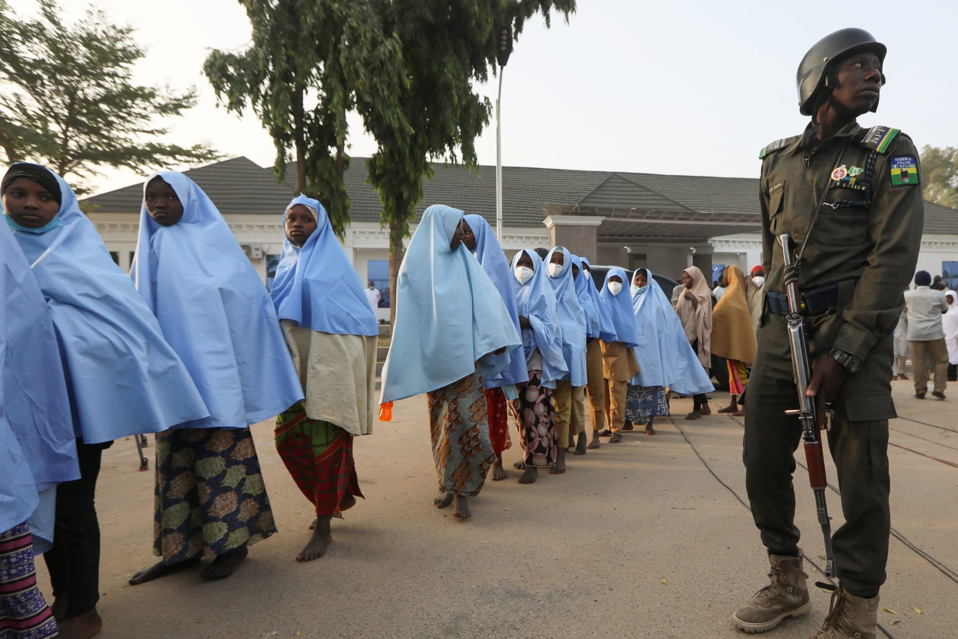 <p>Girls who were kidnapped from a boarding school in the northwest Nigerian state of Zamfara walk in line after their release, as a police officer stands close in Zamfara, Nigeria on March 2, 2021.</p>
