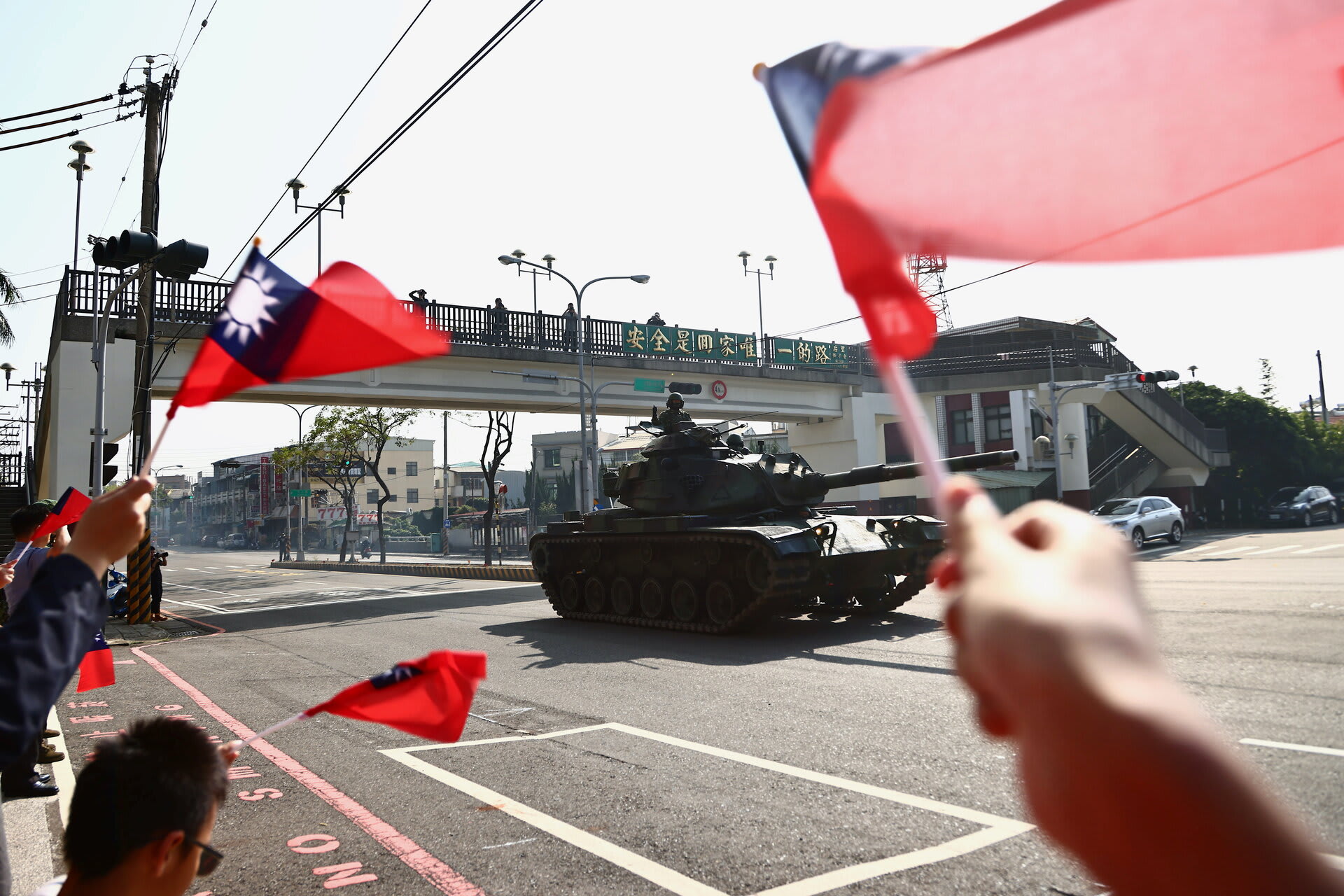 <p>People wave flags while soldiers driving tanks pass on a street as part of a military drill in Taichung, Taiwan, on November 3, 2020.</p>
