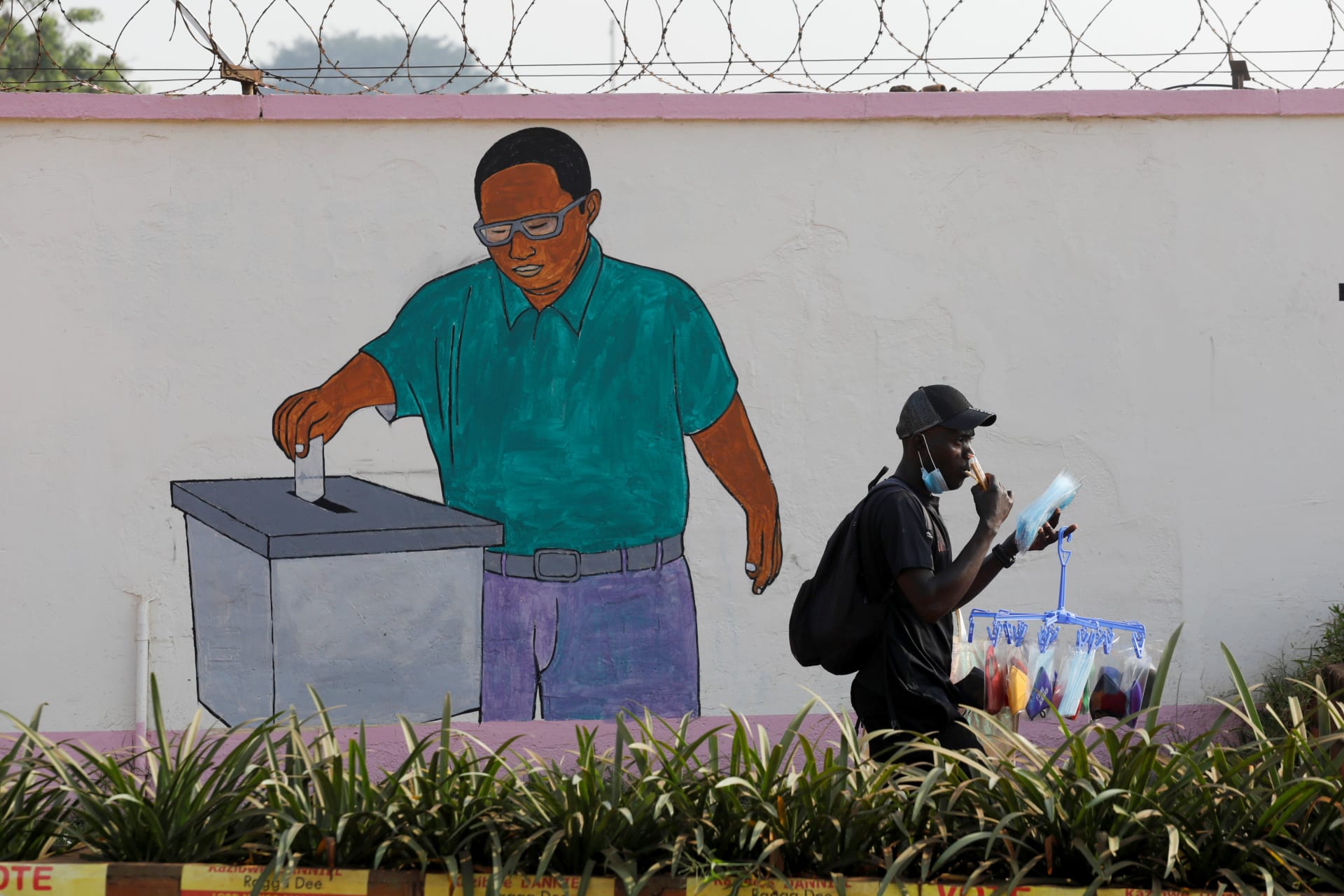 <p>A man walks past a painting on the wall of the Ugandan electoral commission compound in Kampala, Uganda January 13, 2021</p>

