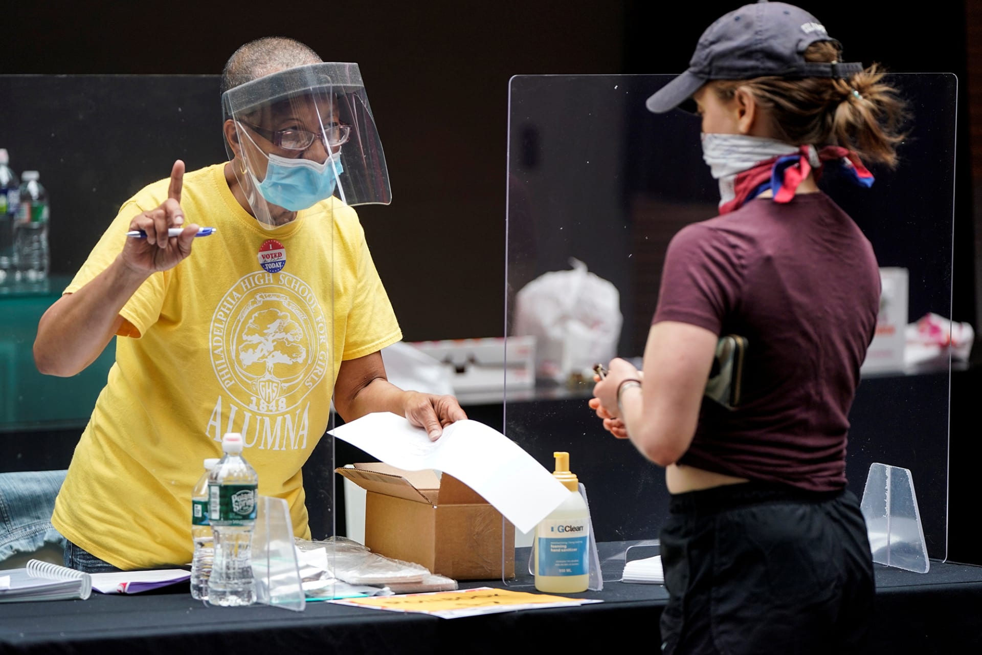 <p>A poll worker and voter wear masks to prevent the spread of COVID-19 during a U.S. primary election.</p>
