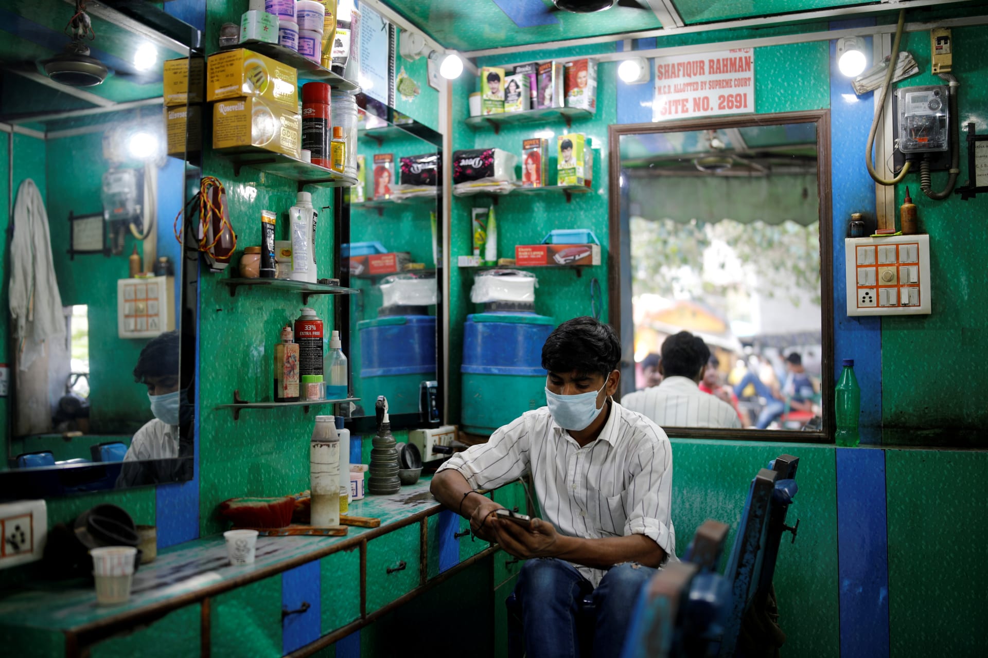 <p>A barber wearing a protective face mask looks at his mobile phone.</p>
