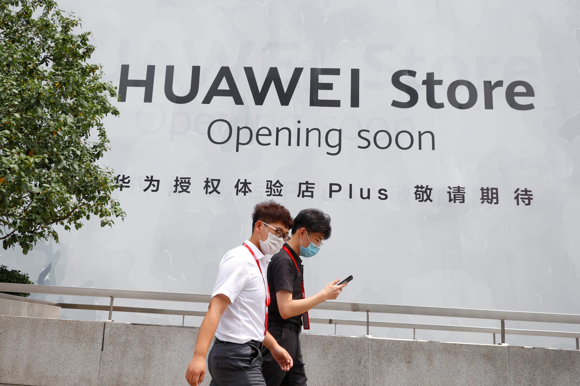 <p>People walk past an advertisement announcing the opening of a Huawei store.</p>

