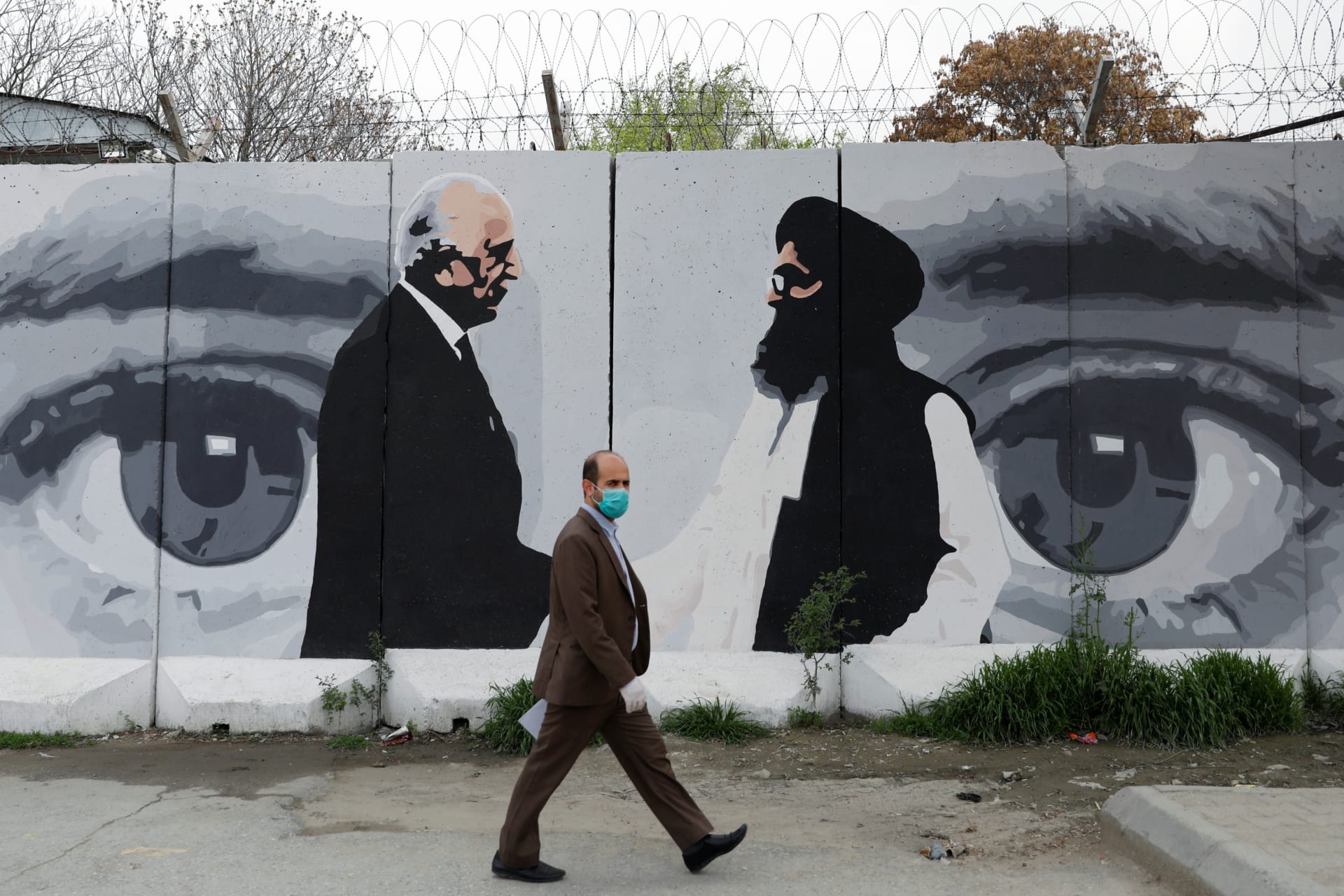 <p>An Afghan man walks past a wall painted with a photo of U.S. Special Representative for Afghanistan Reconciliation Zalmay Khalilzad in Kabul, Afghanistan, on April 13, 2020.</p>
