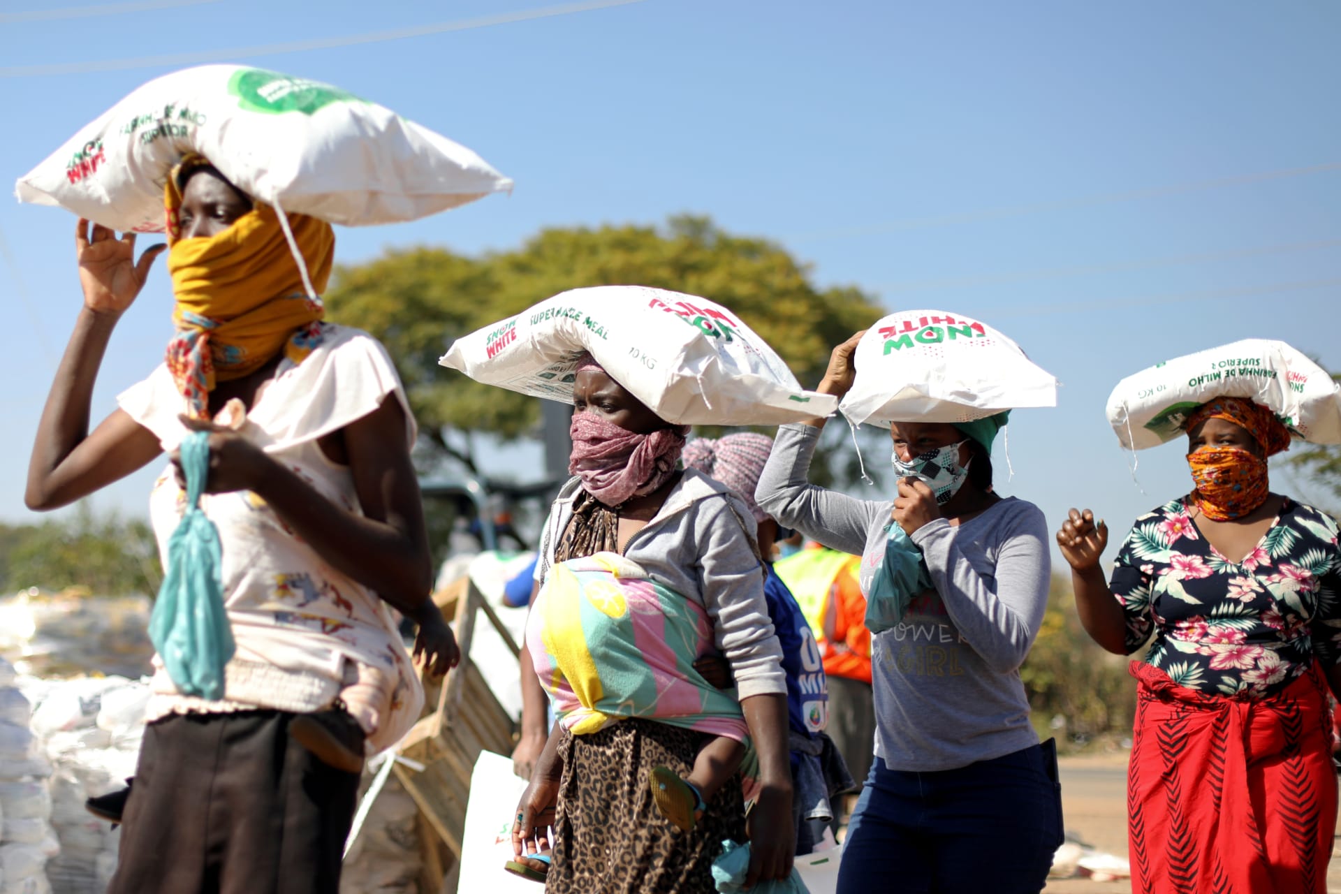 <p>Women carry bags of maize as people queue to receive food aid amid the spread of the novel coronavirus, near Pretoria, South Africa, on May 20, 2020.</p>
