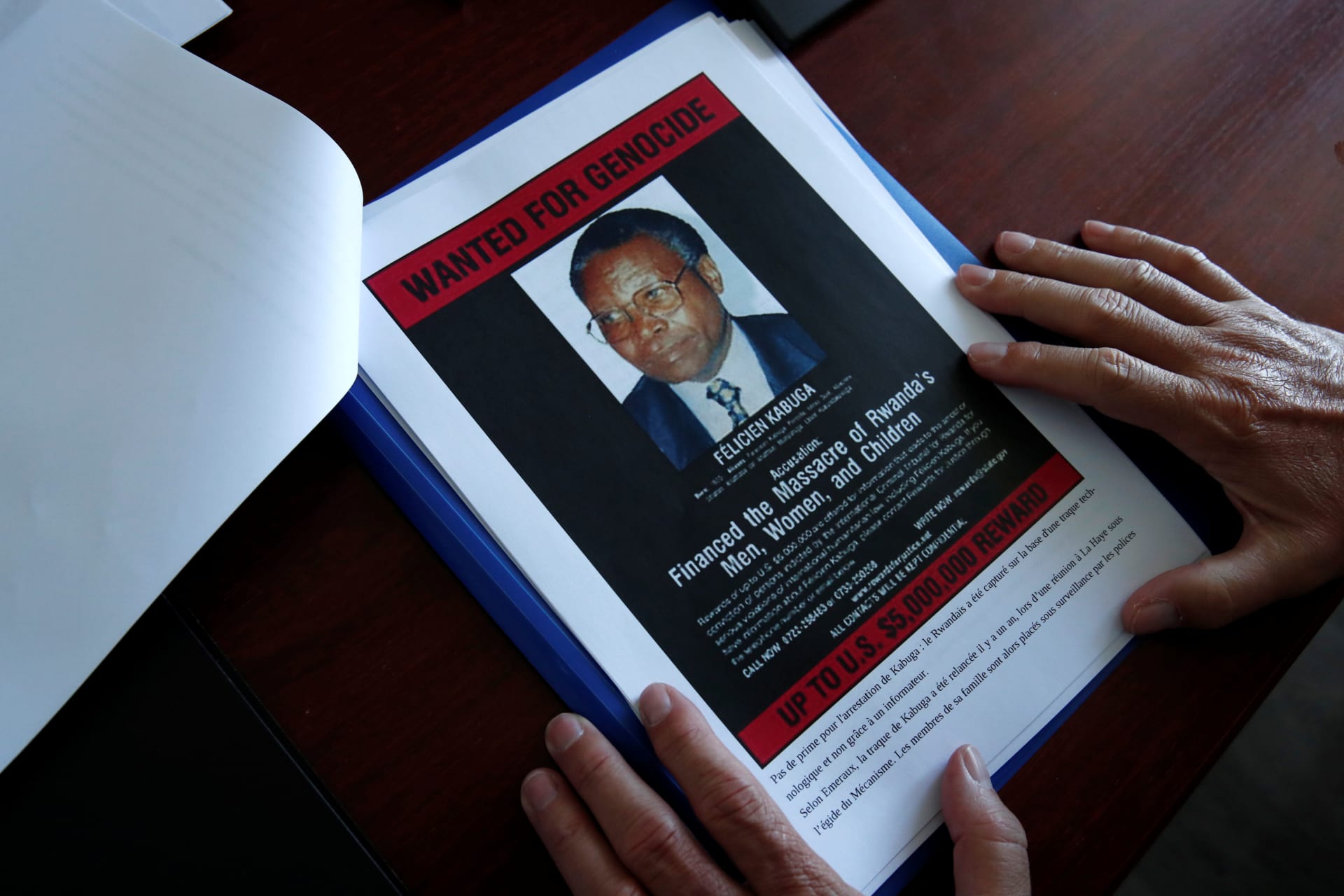 <p>The head of the Gendarmerie’s Central Office for Combating Crimes Against Humanity, Genocides and War Crimes (OCLCH), displays documents with a wanted poster depicting a photograph of Felicien Kabuga, May 19, 2020</p>
