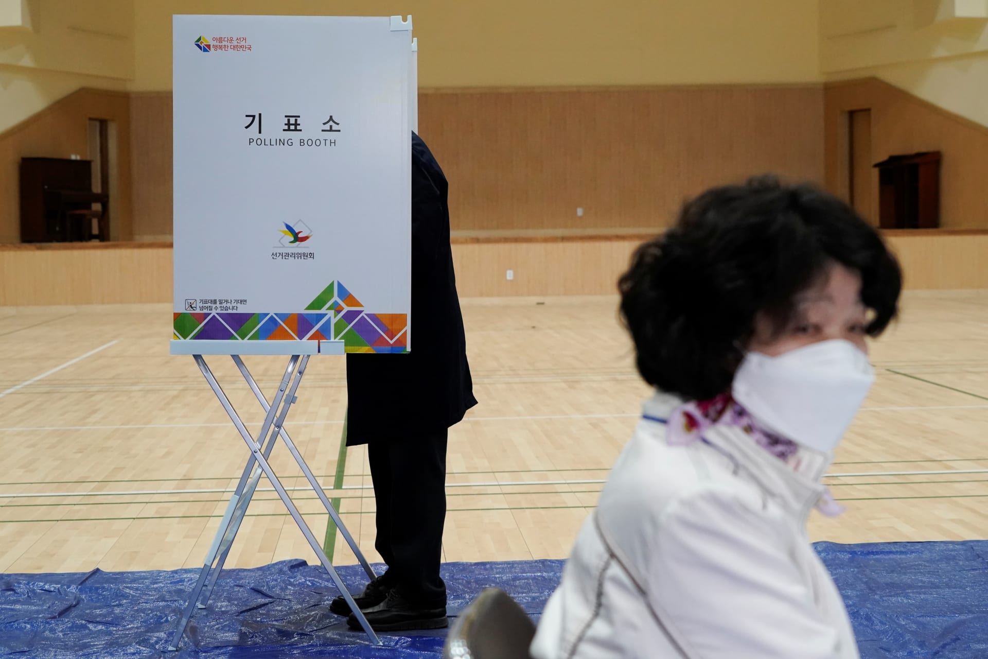 <p>A woman wearing a face mask in an effort to prevent the spread of the coronavirus disease (COVID-19), walks past a voter at a polling booth in Seoul, South Korea, on April 15, 2020.</p>

