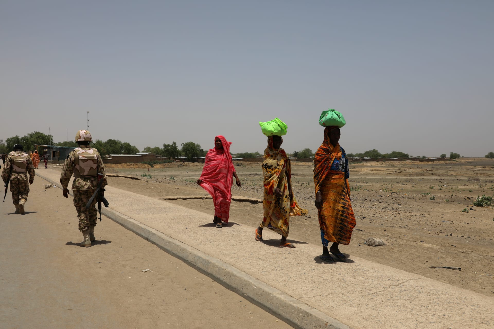 <p>Women walk past soldiers on a bridge separating Cameroon and Nigeria, in Gamboru Ngala, Borno, Nigeria, on April 27, 2017</p>
