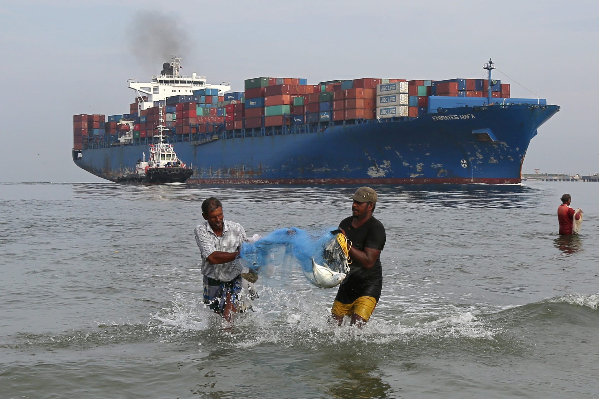 <p>Fishermen carry bluefin trevally fish, locally known as Vatta, as a cargo ship carries containers in the Arabian Sea off Kochi, India, on May 9, 2018. </p>
