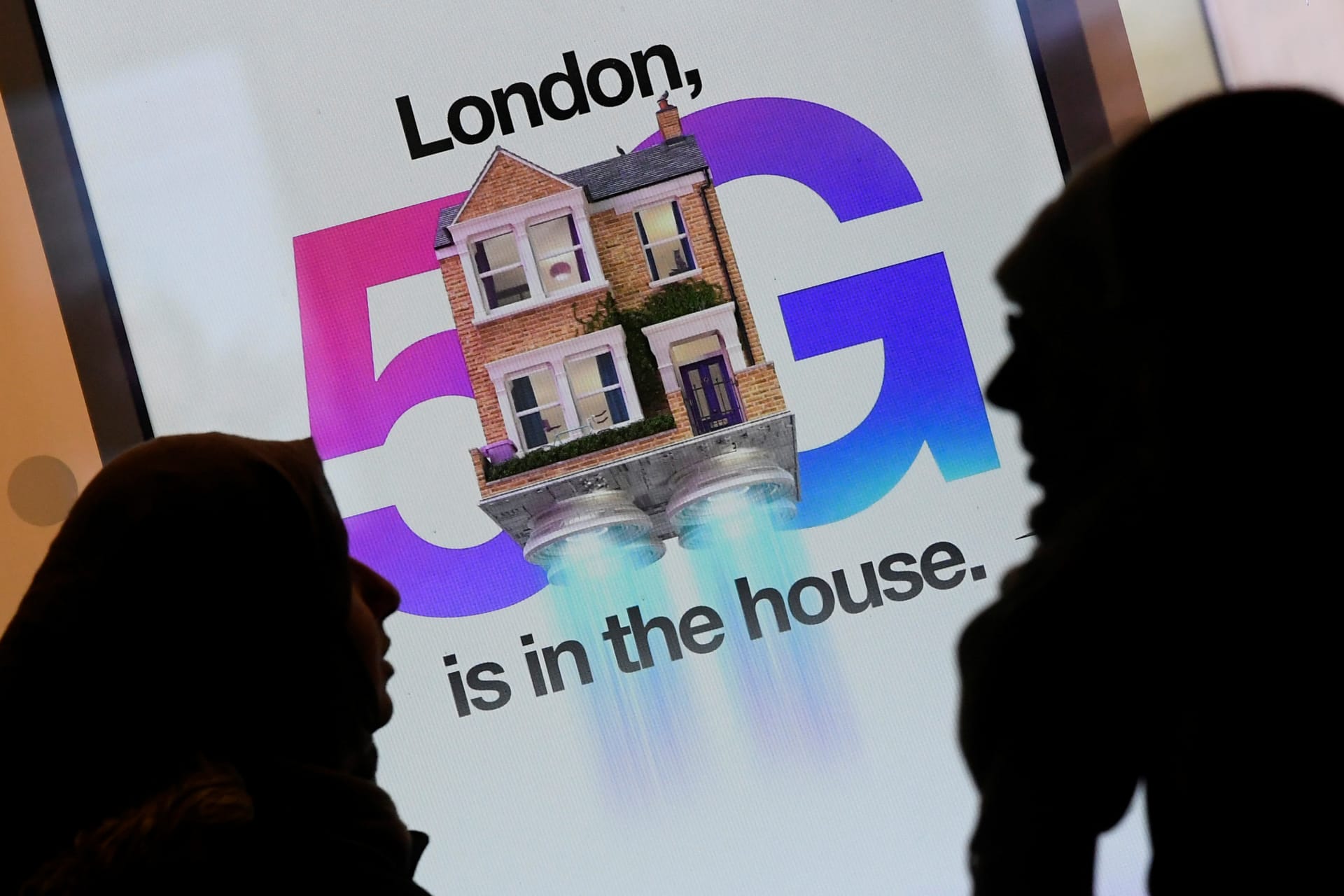 <p>Pedestrians walk past an advertisement promoting the 5G data network at a mobile phone store in London</p>
