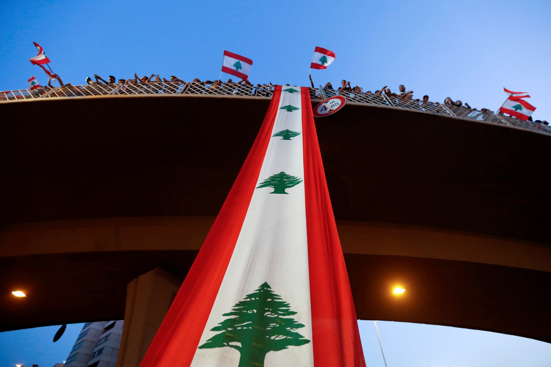 <p>Demonstrators stand on a bridge decorated with a national flag during an anti-government protest along a highway in Lebanon, on October 21, 2019.</p>
