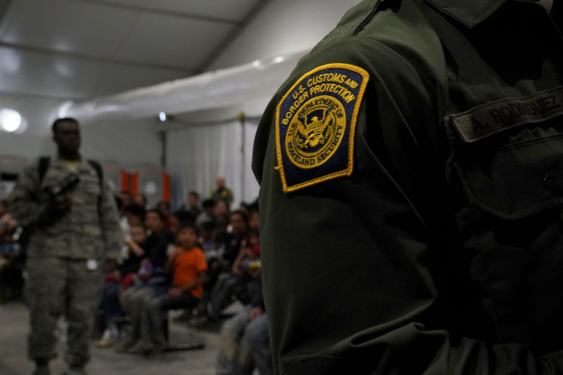 <p>A U.S. Customs and Border Patrol officer stands by migrants at a processing facility in Donna, Texas. </p>
