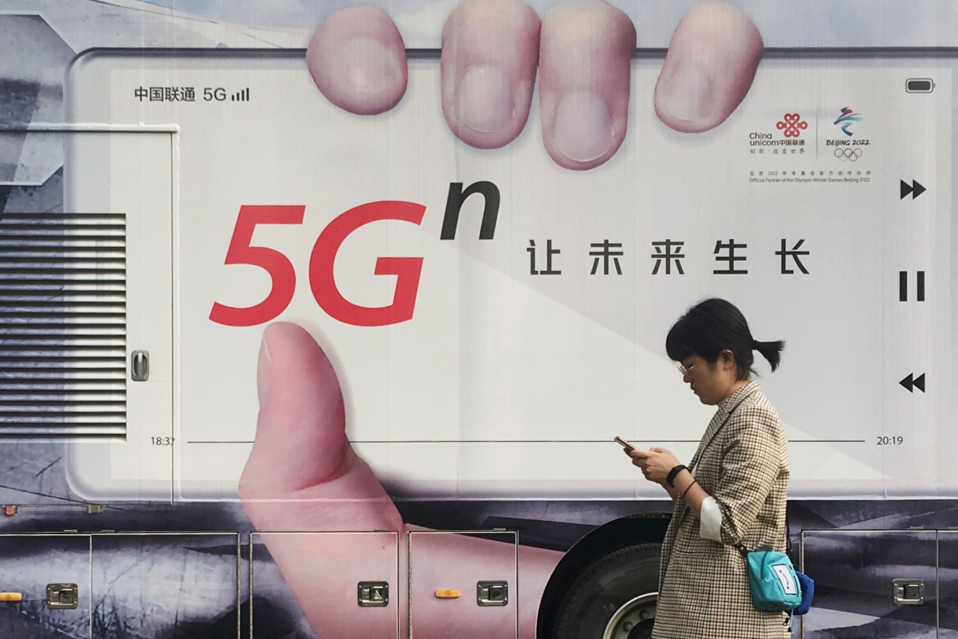 <p>A woman using her mobile phone walks past a vehicle covered in a China Unicom 5G advertisement in Beijing, China September 17, 2019.</p>

