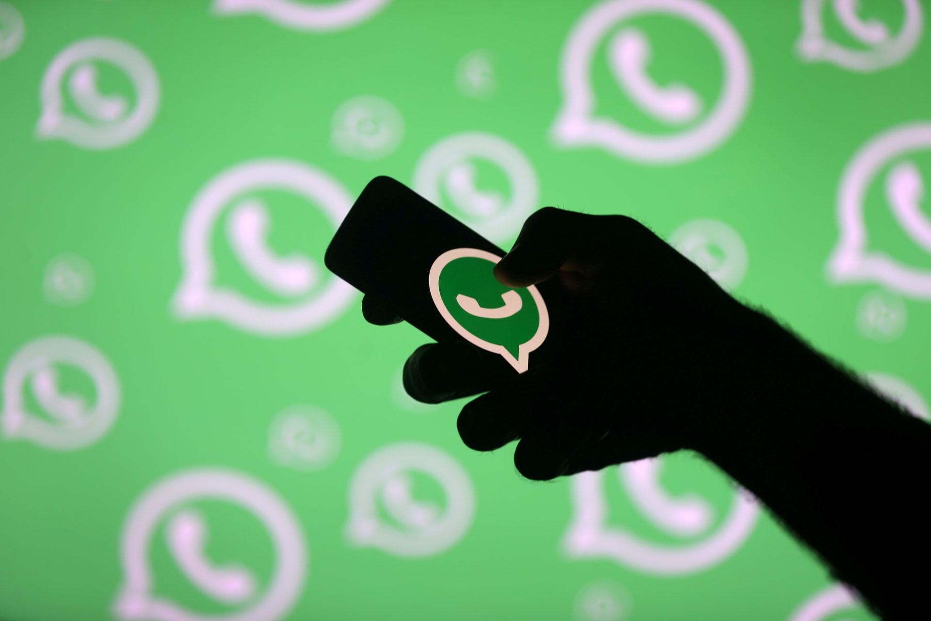 <p>A man poses with a smartphone in front of displayed Whatsapp logo in this illustration</p>
