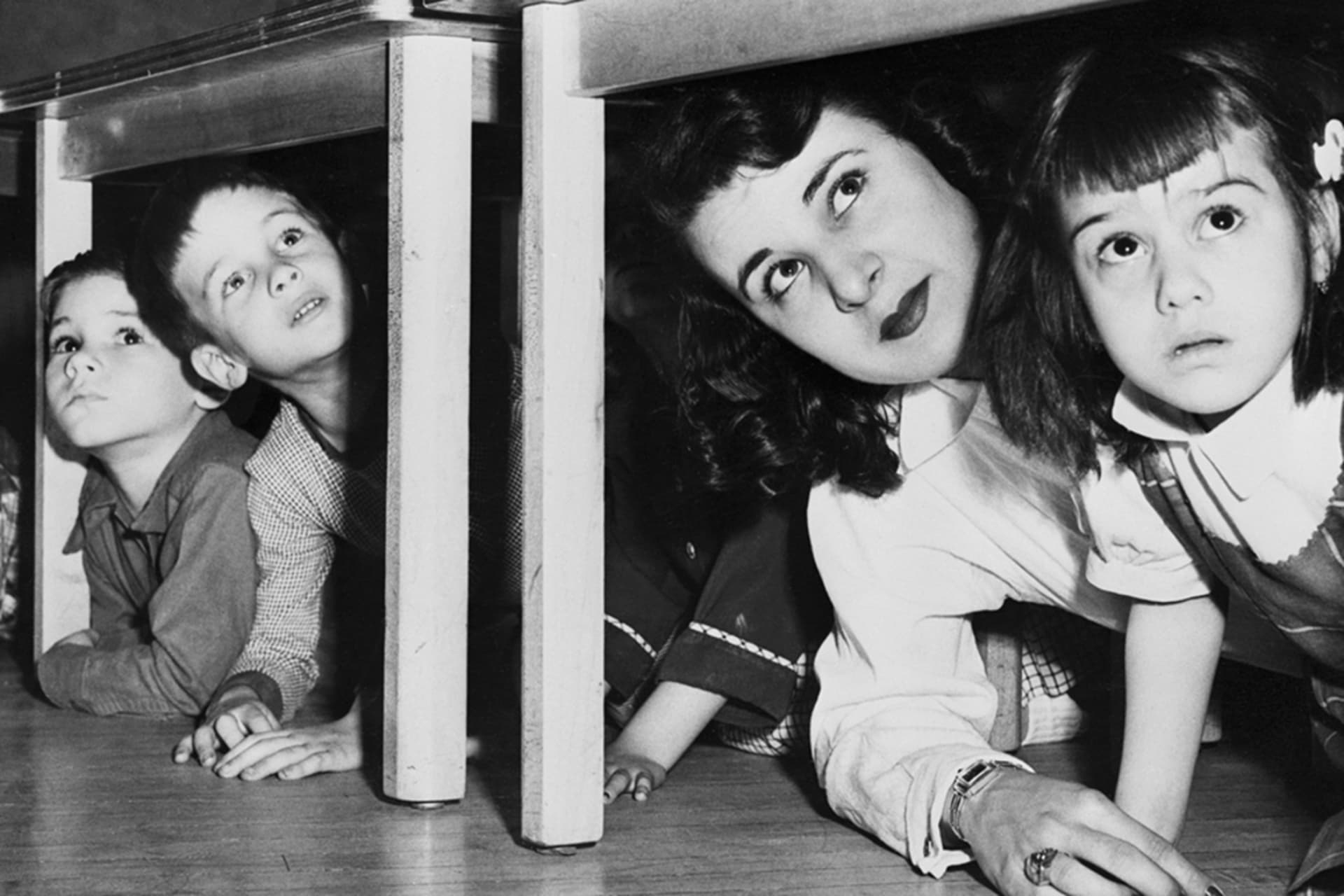 <p>School children and their teacher peer from beneath the table during New Jersey’s first state-wide air raid test.</p>
