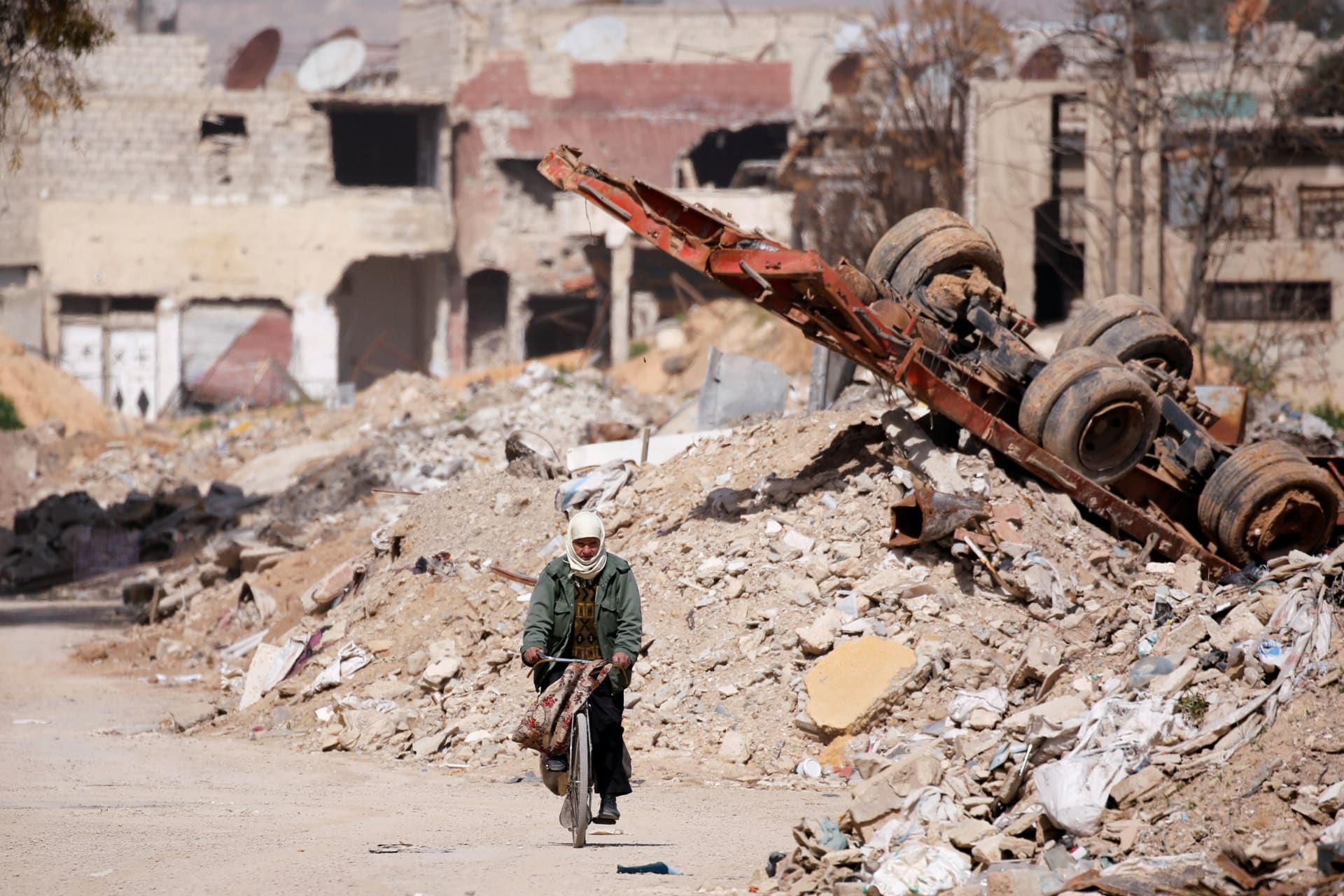 <p>A man rides on a bike past rubble in Ein Terma, a district of eastern Ghouta, Syria, on February 26, 2019</p>

