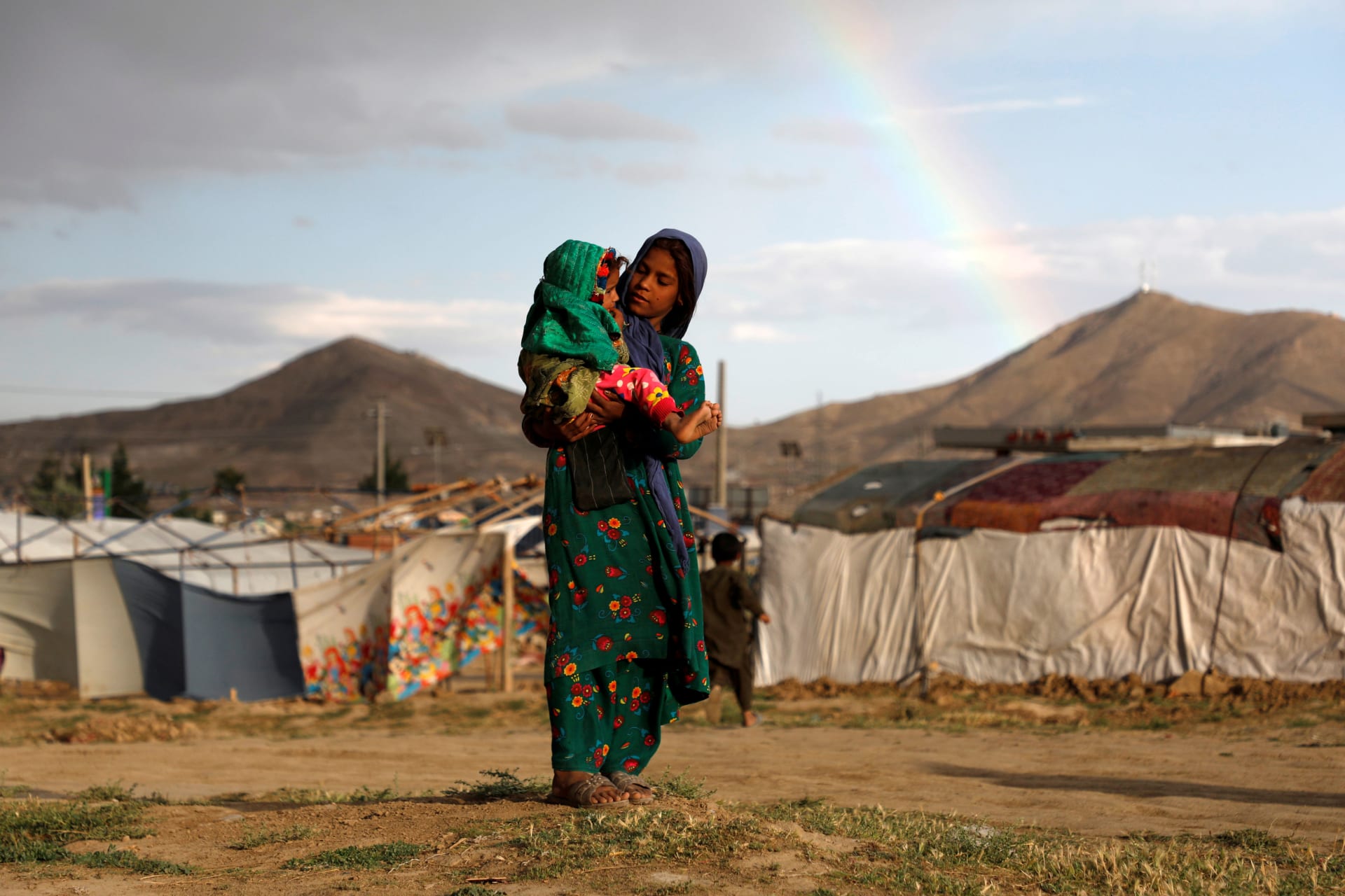 <p>An internally displaced Afghan girl carries a child near their shelter at a refugee camp on the outskirts of Kabul, Afghanistan, on June 20, 2019.</p>
