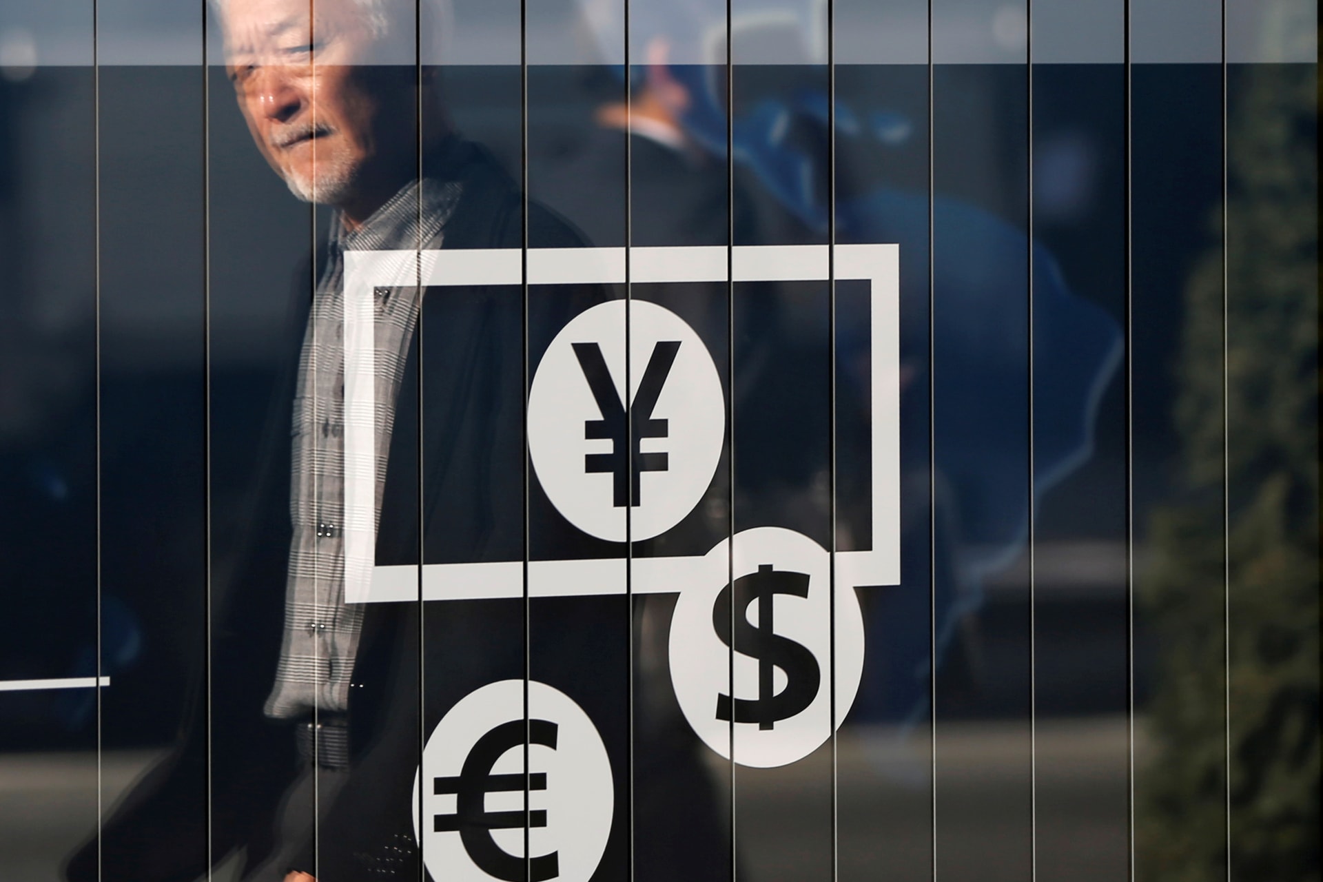 <p>Passers-by are reflected on a signboard displaying currency signs outside a bank in Tokyo November 27, 2014. </p>
