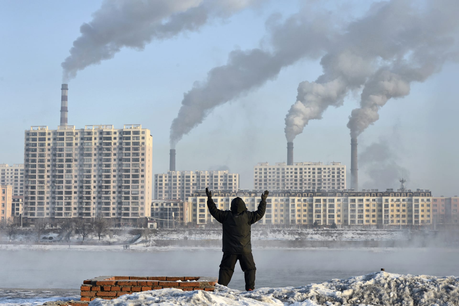 <p>An elderly man exercises in the morning as he faces chimneys emitting smoke behind buildings across the Songhua river in Jilin province, China on February 24, 2013</p>
