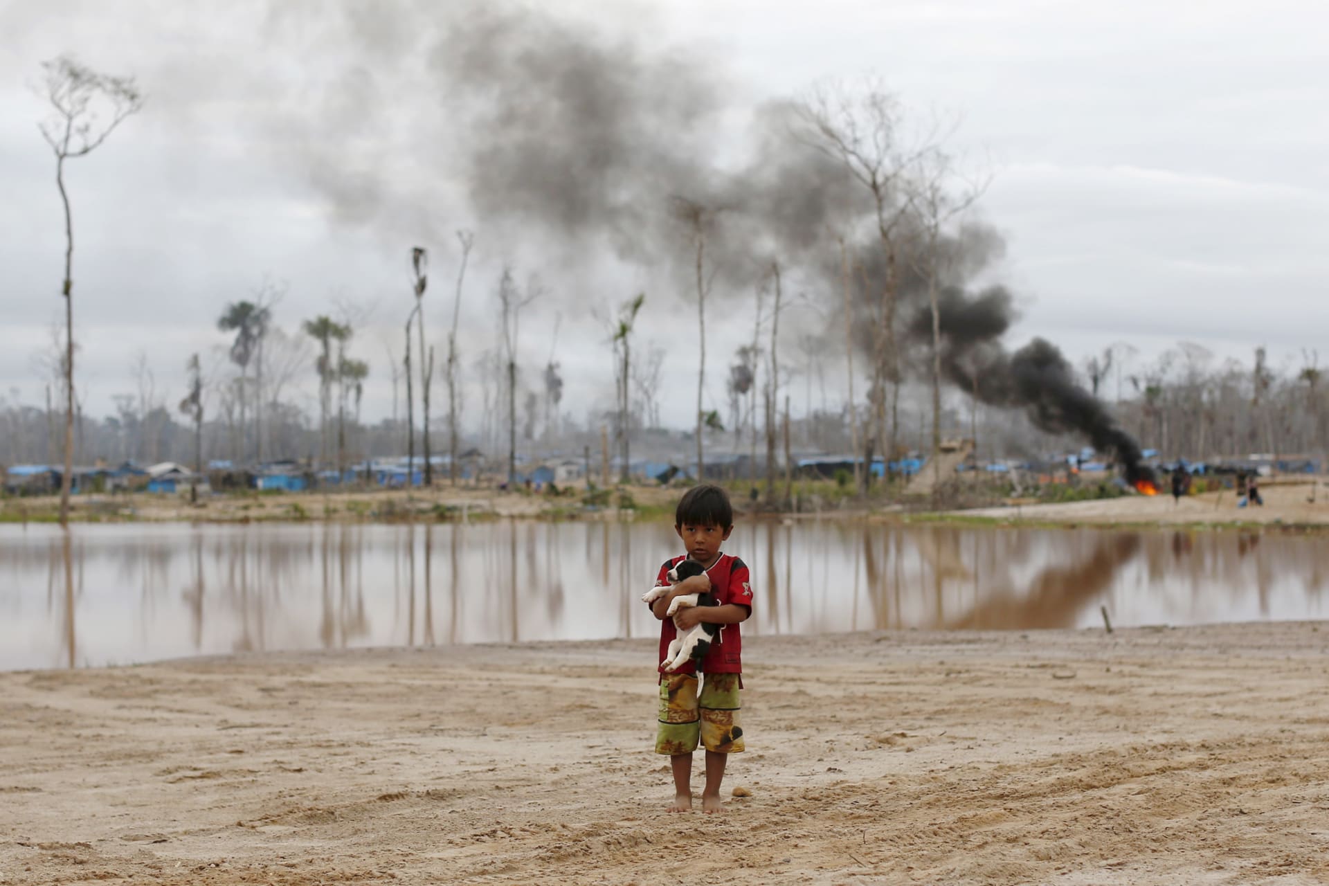 <p>A boy carries a dog as he stands after a Peruvian police operation to destroy illegal gold mining camps in the southern Amazon region of Madre de Dios on July 14, 2015. </p>
