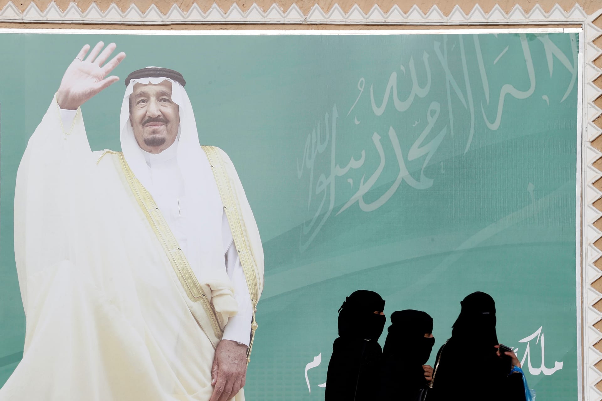 <p>Women walk past a poster of Saudi Arabia’s King Salman bin Abdulaziz Al Saud.</p>