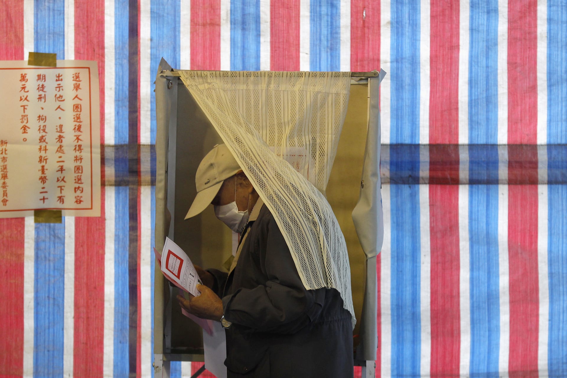 <p>A man wearing a health mask walks out of a voting booth in Xinbei, Taiwan. </p>
