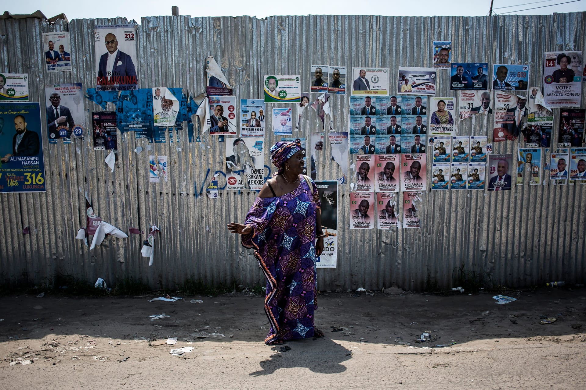 <p>A woman signals for a taxi in front of a wall filled with campaign posters in Kinshasa.</p>
