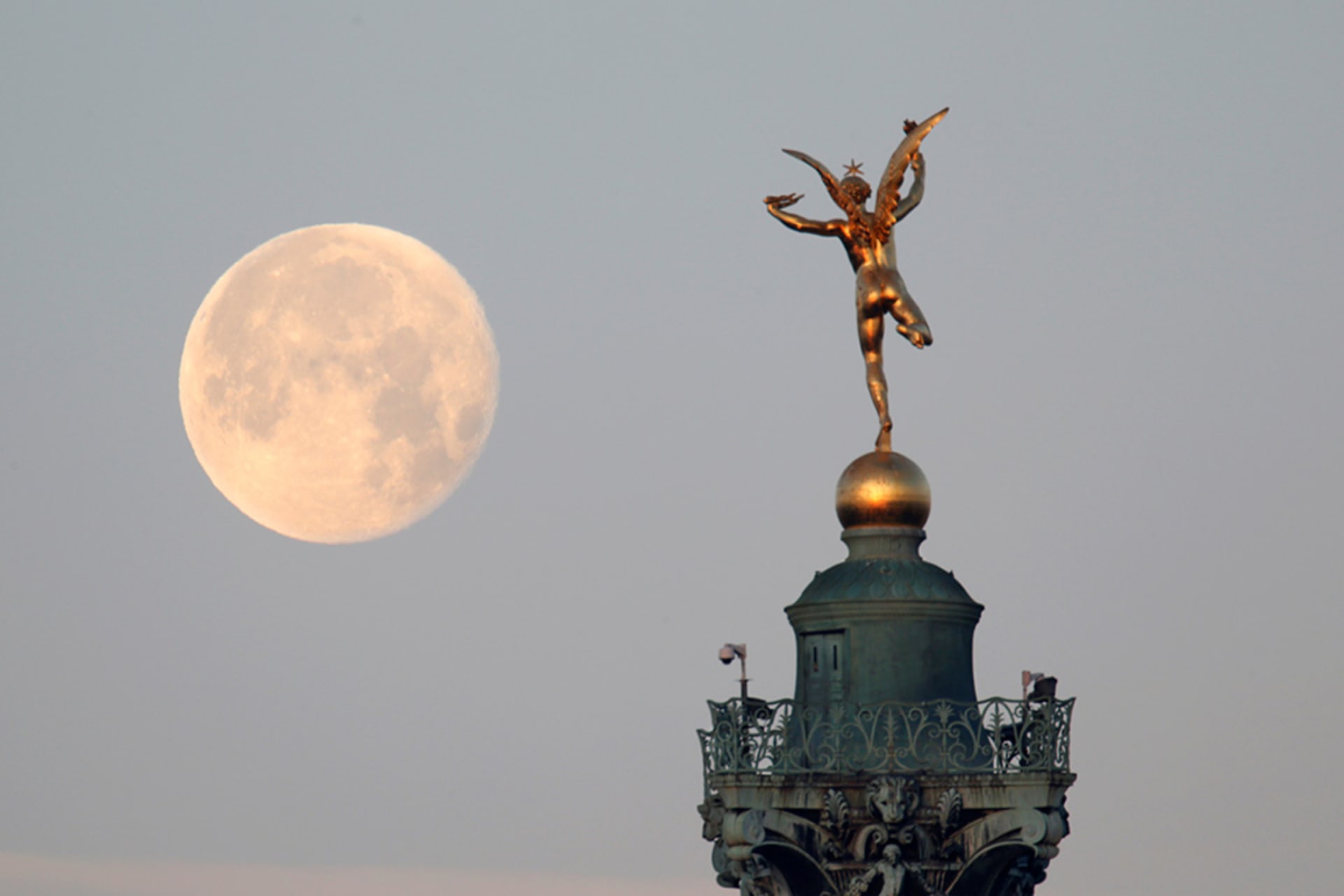 <p>The moon is seen behind the Genie de la Liberte gilded figure on top of the Place de la Bastille’s July Column in Paris.</p>
