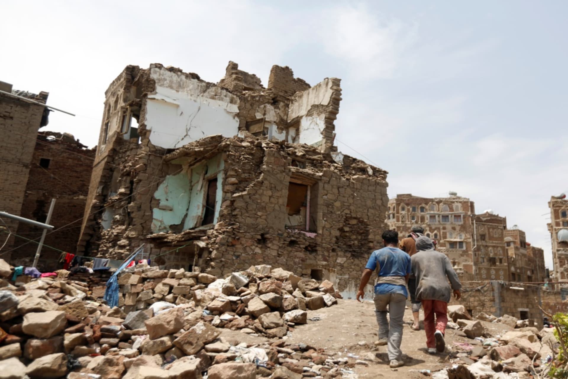<p>People walk past a house destroyed by an air strike in the old quarter of Sanaa, Yemen on August 8, 2018.</p>
