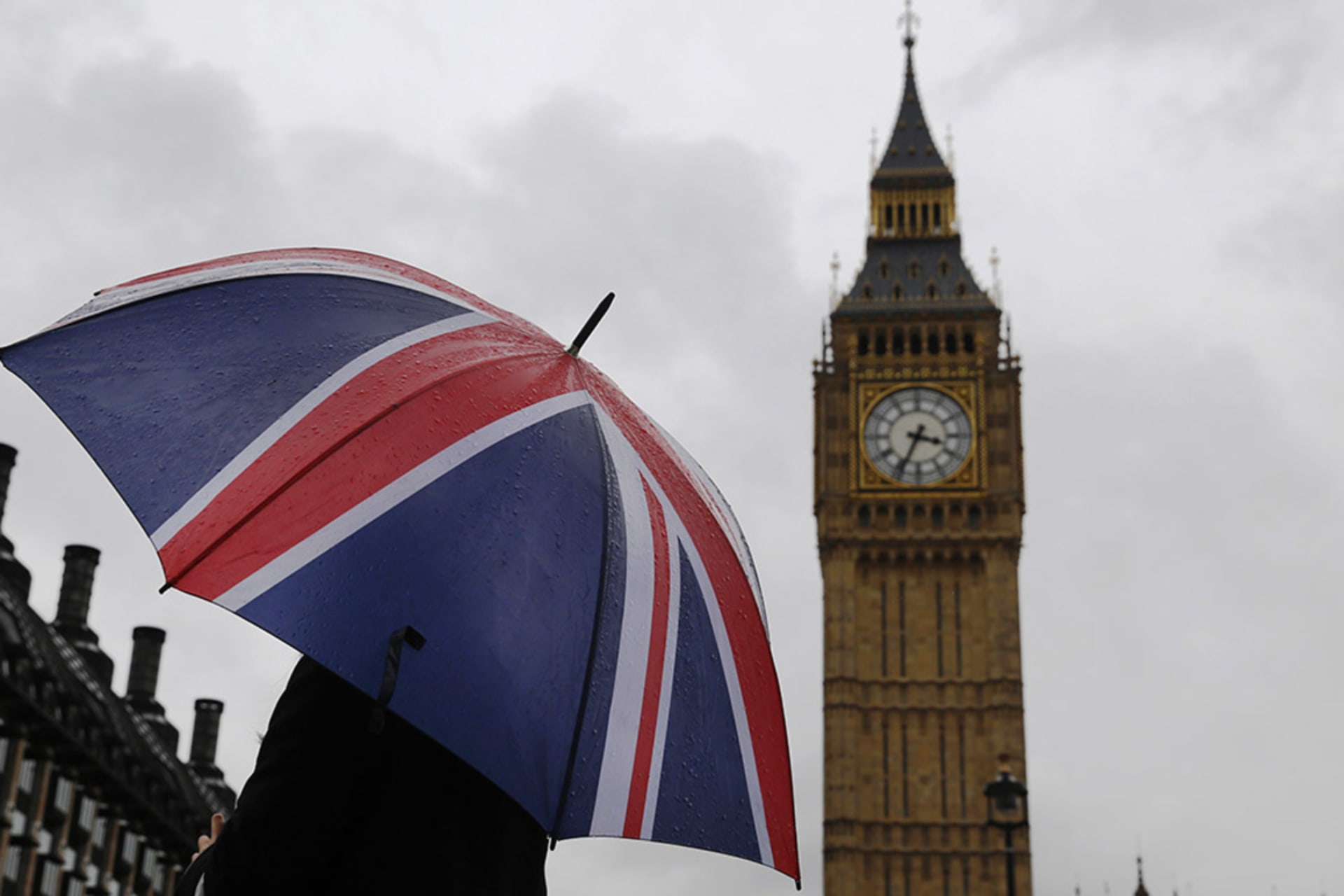 <p>A woman holds a Union flag umbrella in front of the Big Ben clock tower and the Houses of Parliament in London.</p>
