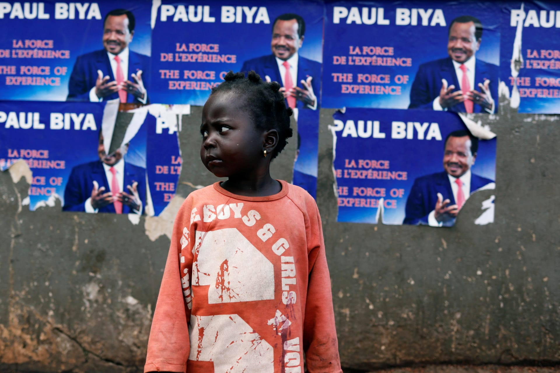 <p>A girl stands near a wall covered with placards of Cameroon President Paul Biya, who was reelected two days later, in Yaounde, Cameroon, on October 5, 2018.</p>
