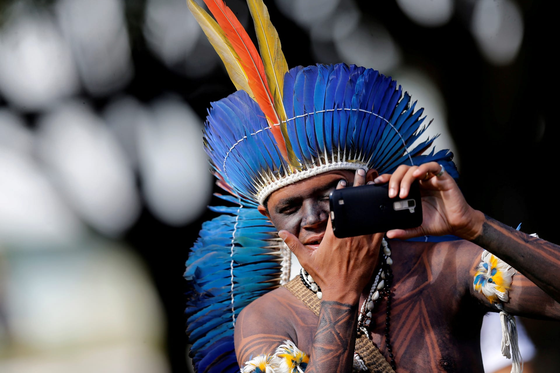 <p>A Brazilian Indigenou checks his face in a mobile phone at the Terra Livre camp, or Free Land camp in Brasilia, Brazil on April 23, 2018</p>