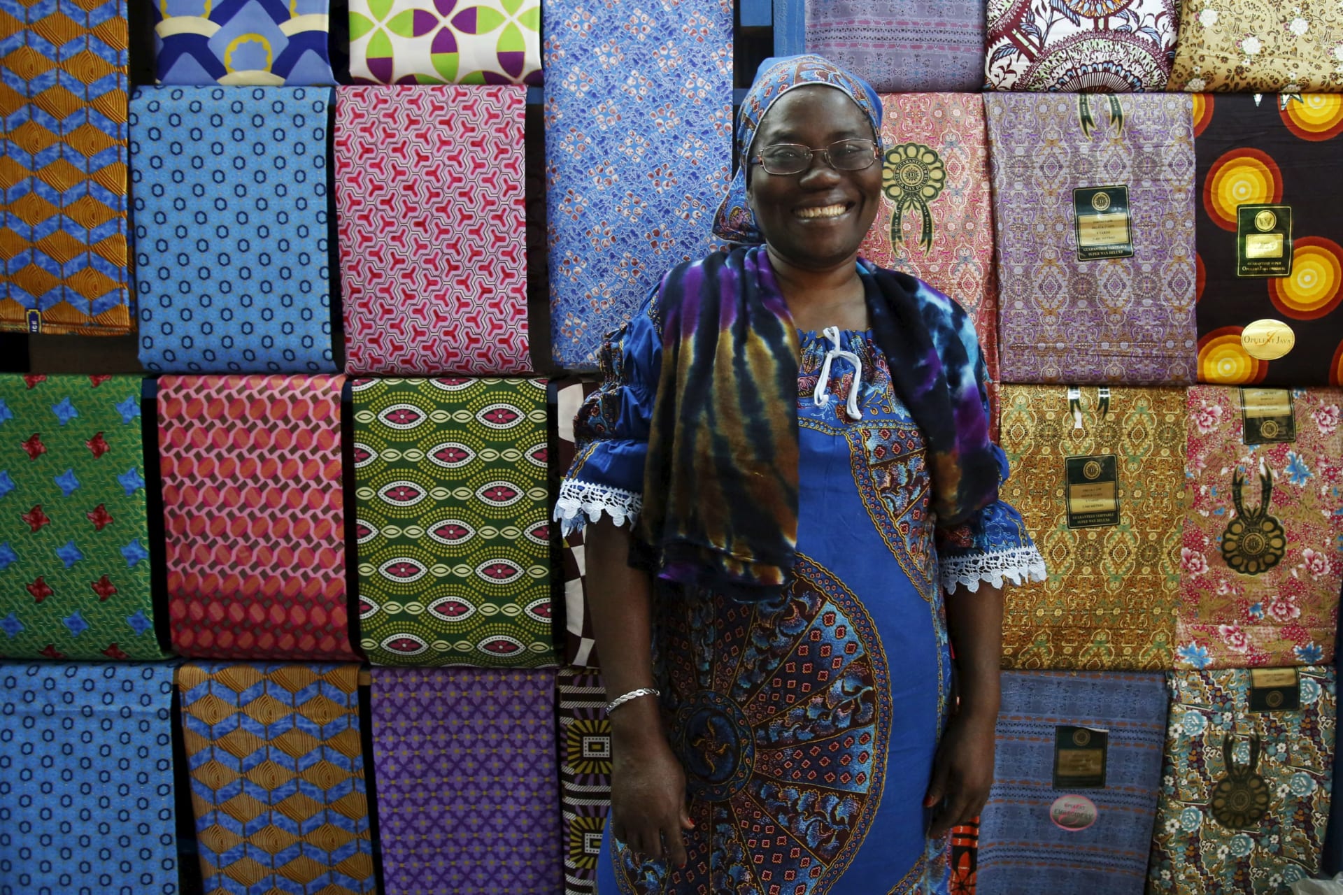 <p>Fofanan Man, a 59-year-old businesswoman, poses for a photograph in front of textiles in her shop in Bouake, Ivory Coast.</p>
