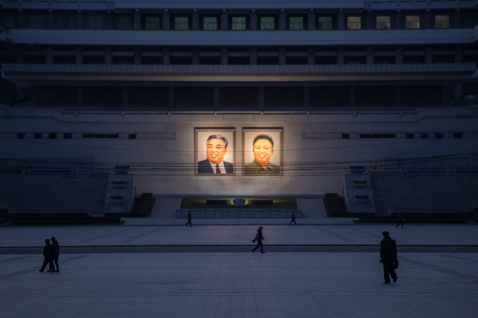 <p>People walk past portraits of Kim Il-sung and Kim Jong-il.</p>
