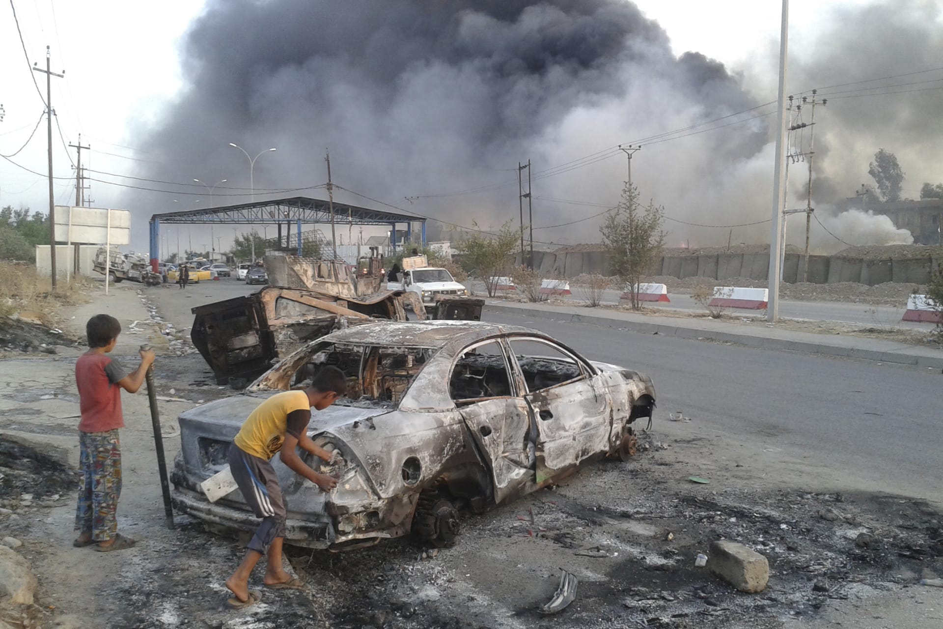 <p>Children stand next to a burnt vehicle during clashes between Iraqi security forces and ISIL in the northern Iraq city of Mosul.</p>
