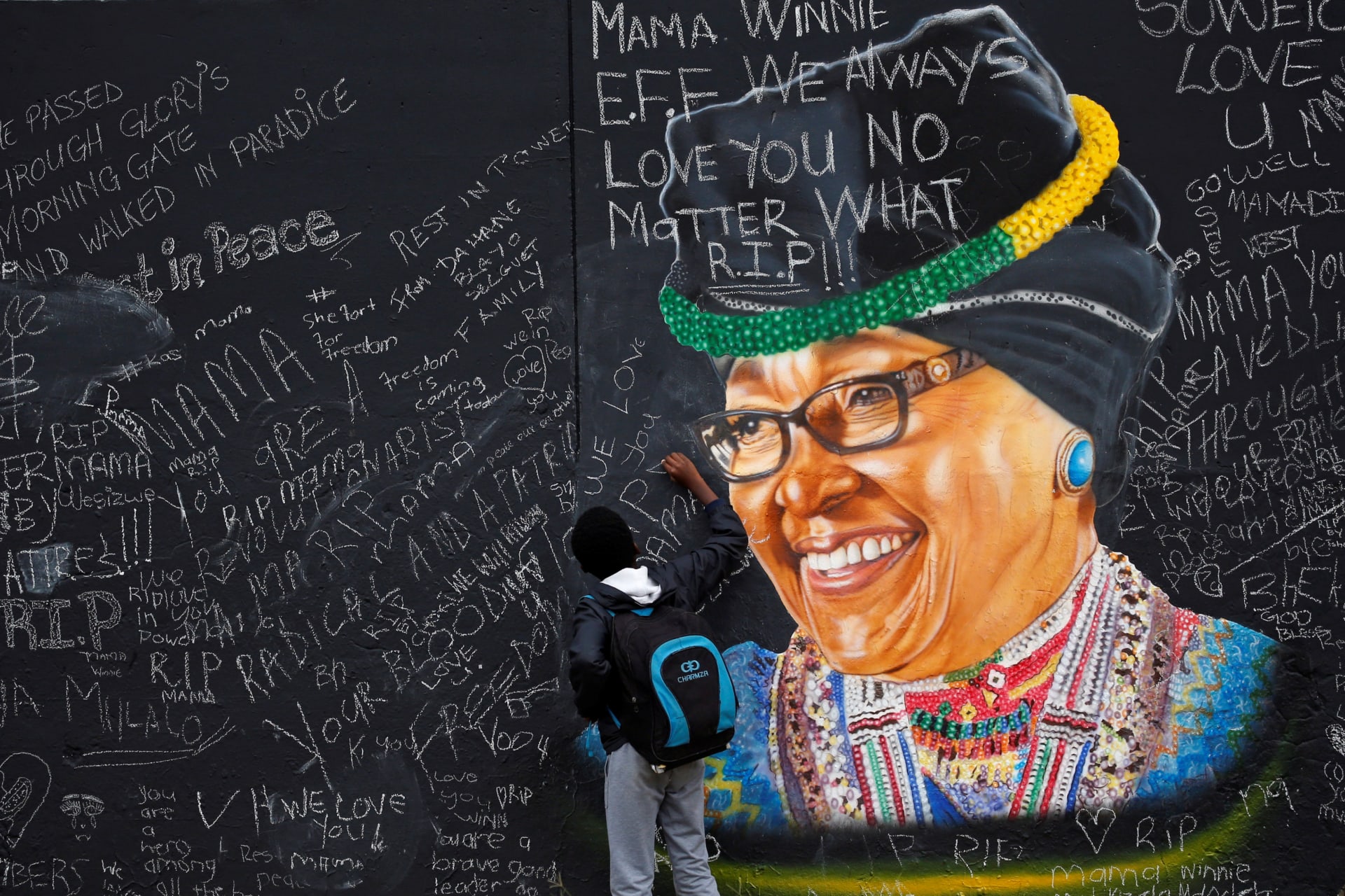 <p>A boy returning from school writes a message on a wall with a mural of the late Winnie Madikizela-Mandela, painted by Inqubeko communications, in Soweto, South Africa, April 13, 2018.</p>

