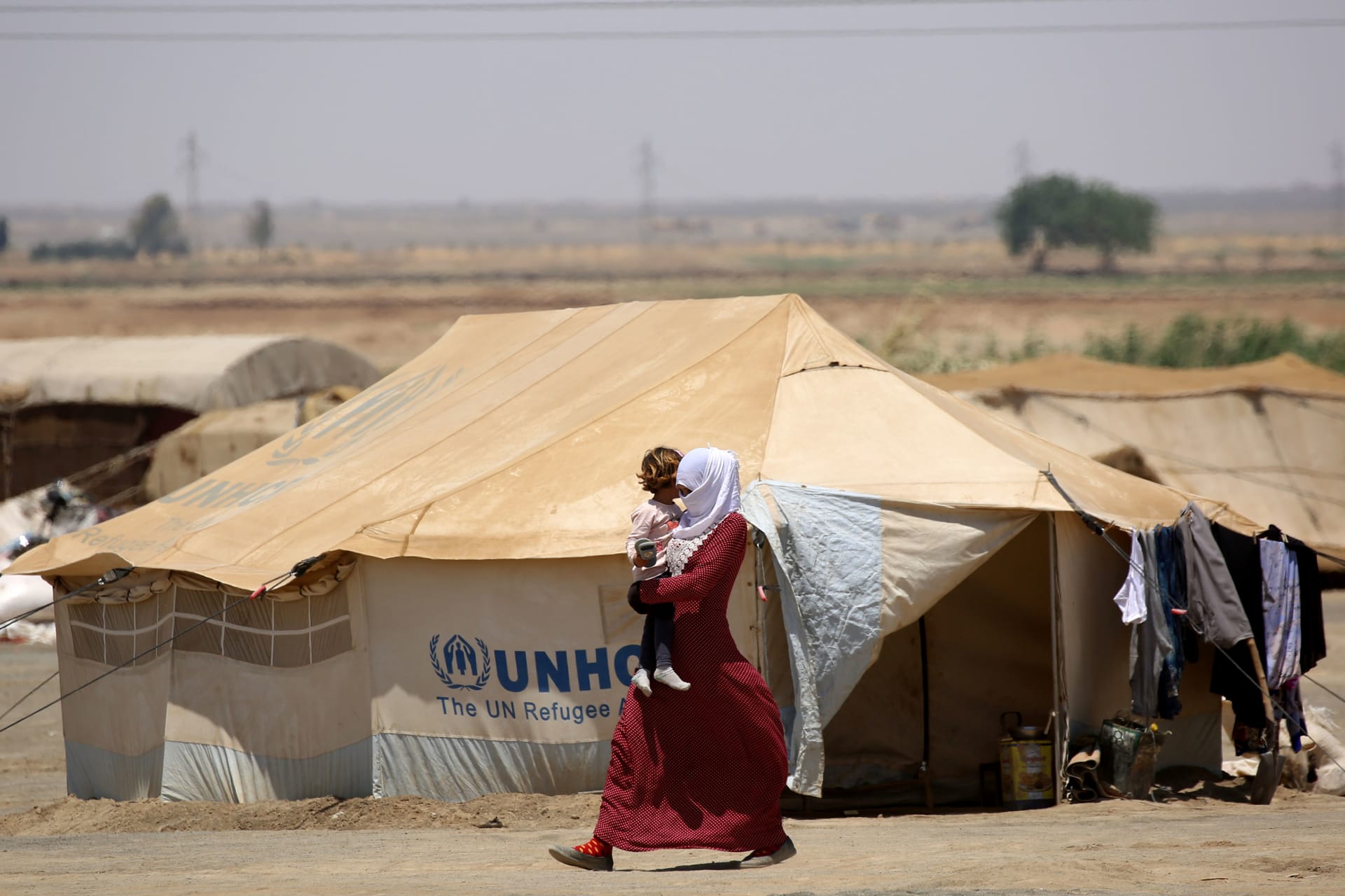 <p>A Syrian woman displaced from Raqa walks carrying a child at the al-Karamah camp</p>
