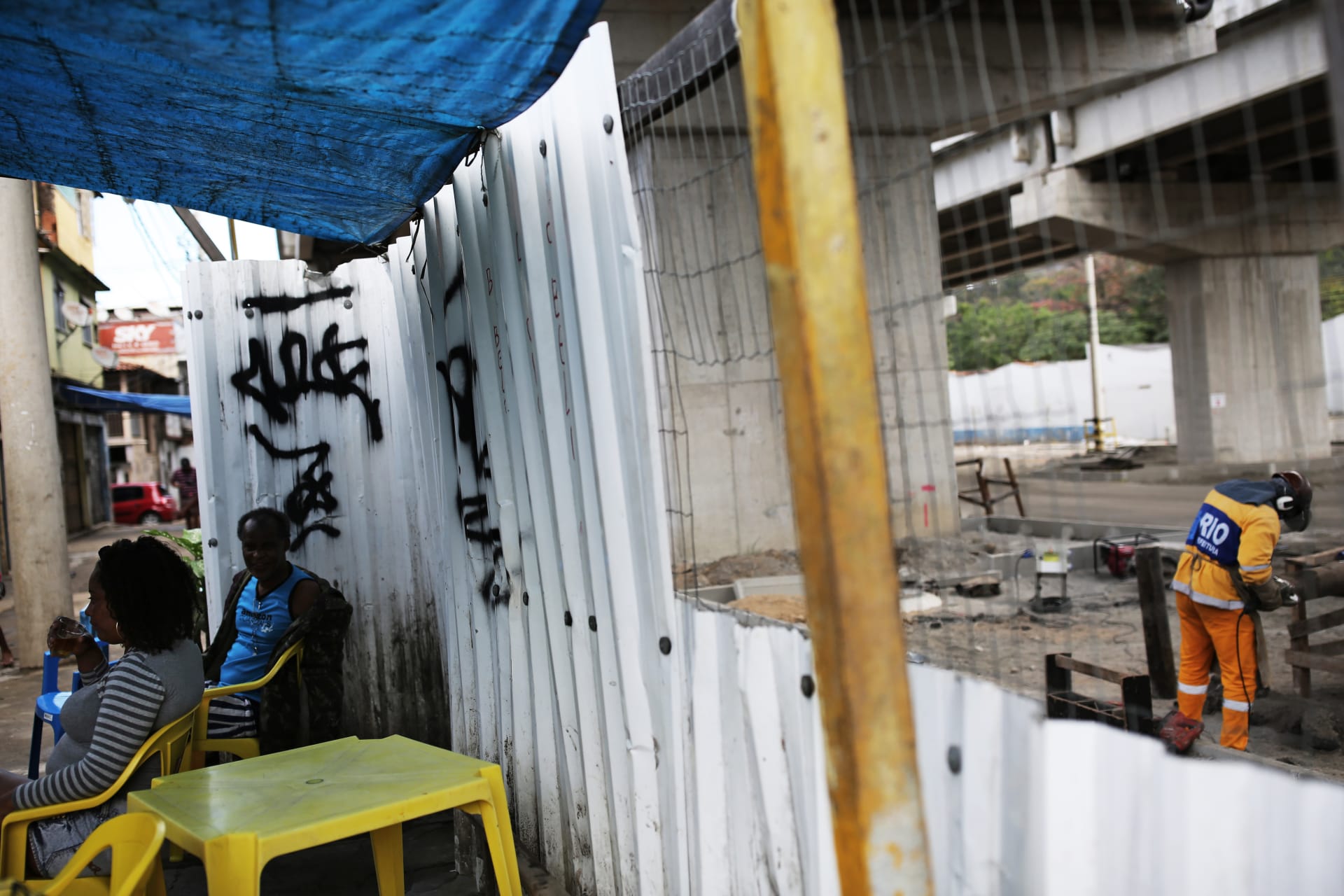 <p>Residents sit behind a divider that separates homes from a bridge of the Transolimpica BRT, an express road built through a shantytown.</p>
