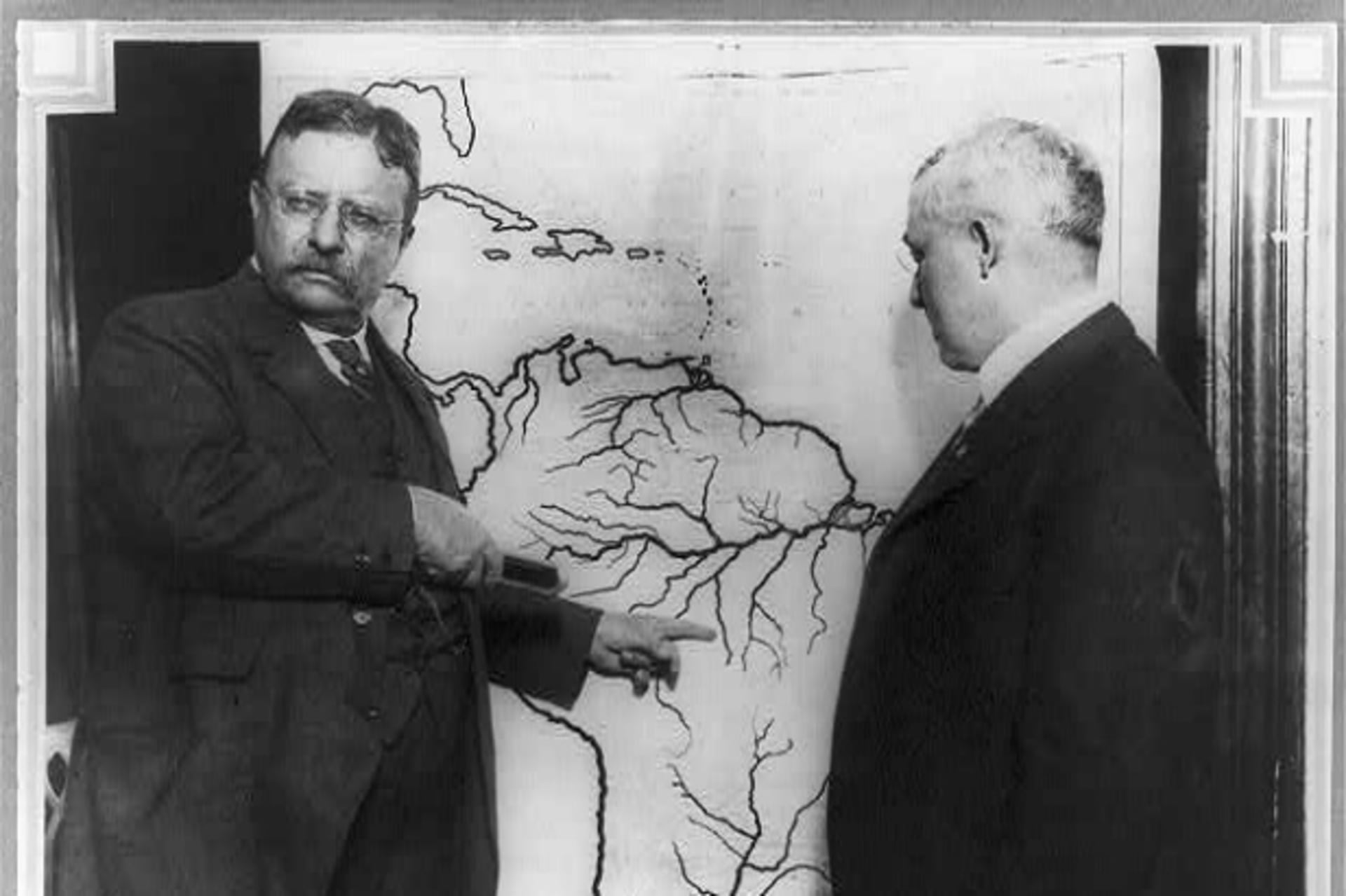 <p>President Roosevelt pointing at a map of South America towards the area explored during the Roosevelt-Rondon Scientific Expedition in Brazil as another man looks on between 1913 and 1919.</p>
